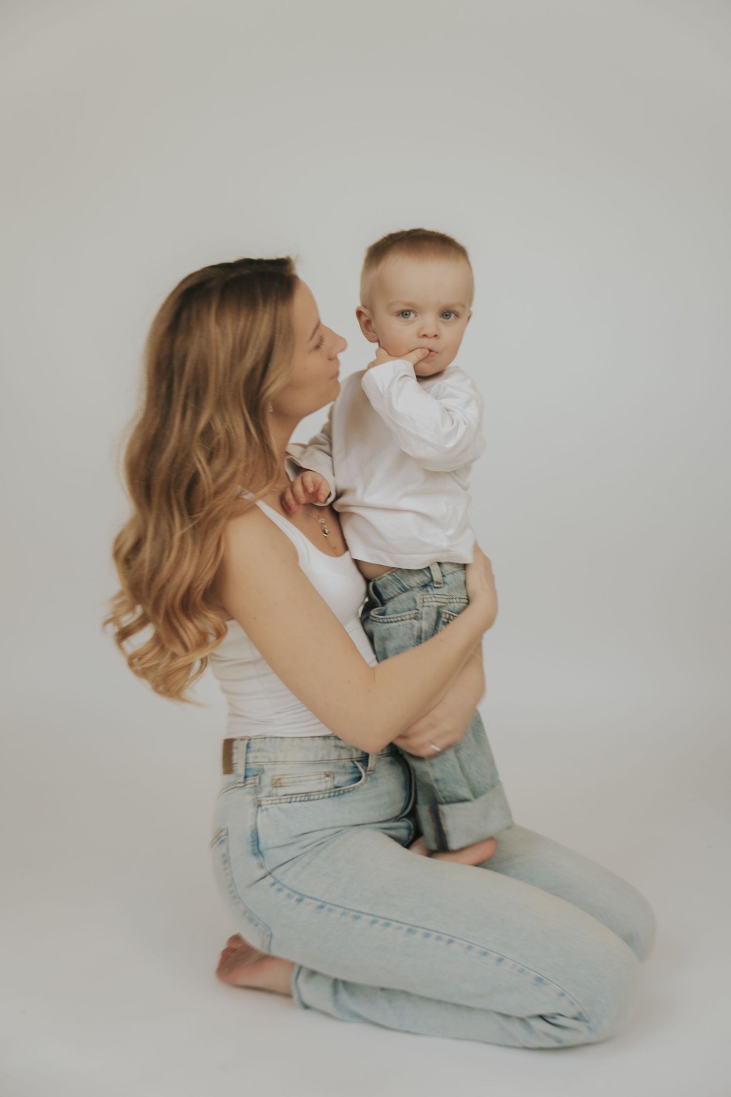 A parent and toddler share a tender moment while posing in denim against a minimalist white background.