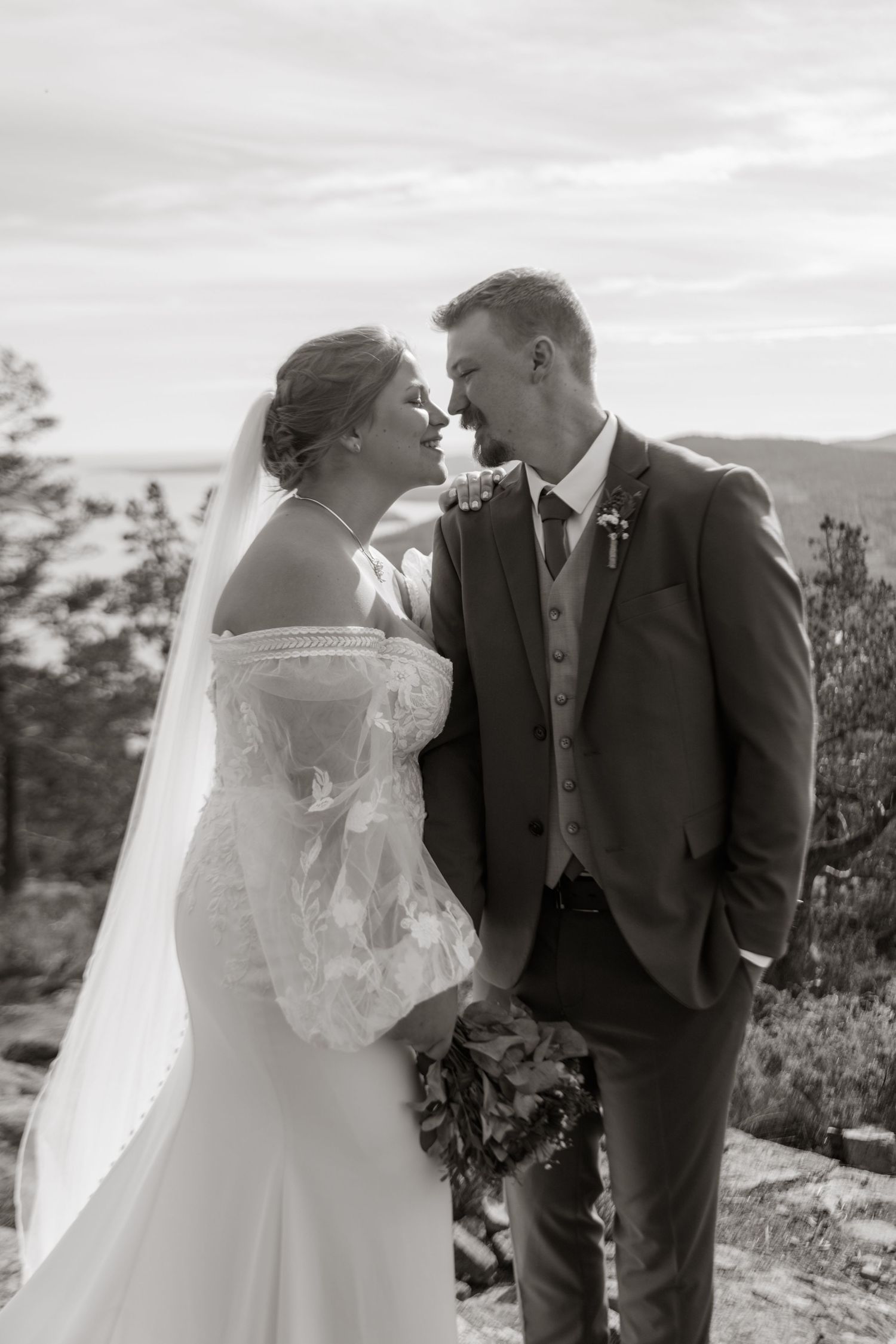 Black and white portrait of wedding couple sharing tender moments on mountain summit.