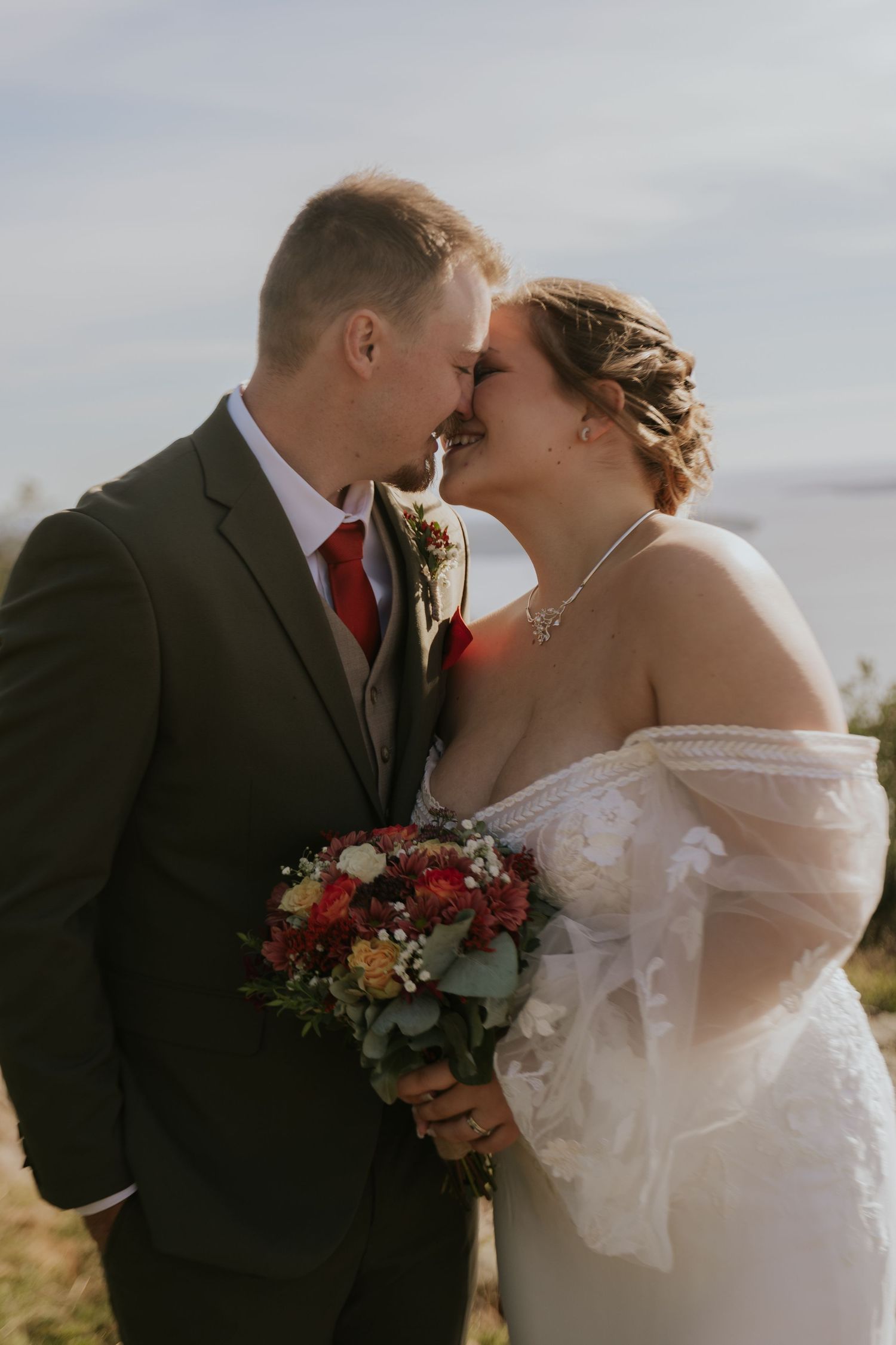 Wedding couple shares intimate moments against mountain backdrop with autumn bouquet.