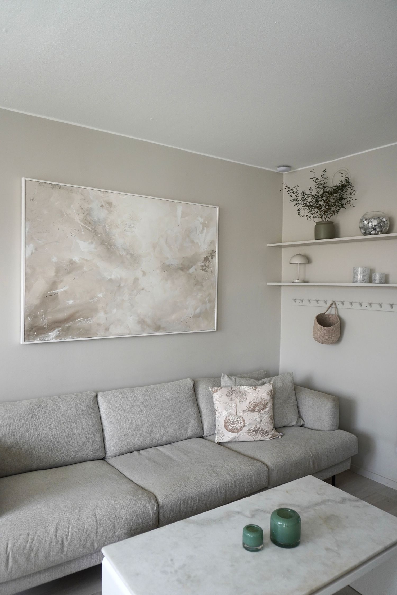 Modern living room interior with grey sectional sofa, abstract wall art, and minimalist decor on floating shelves.