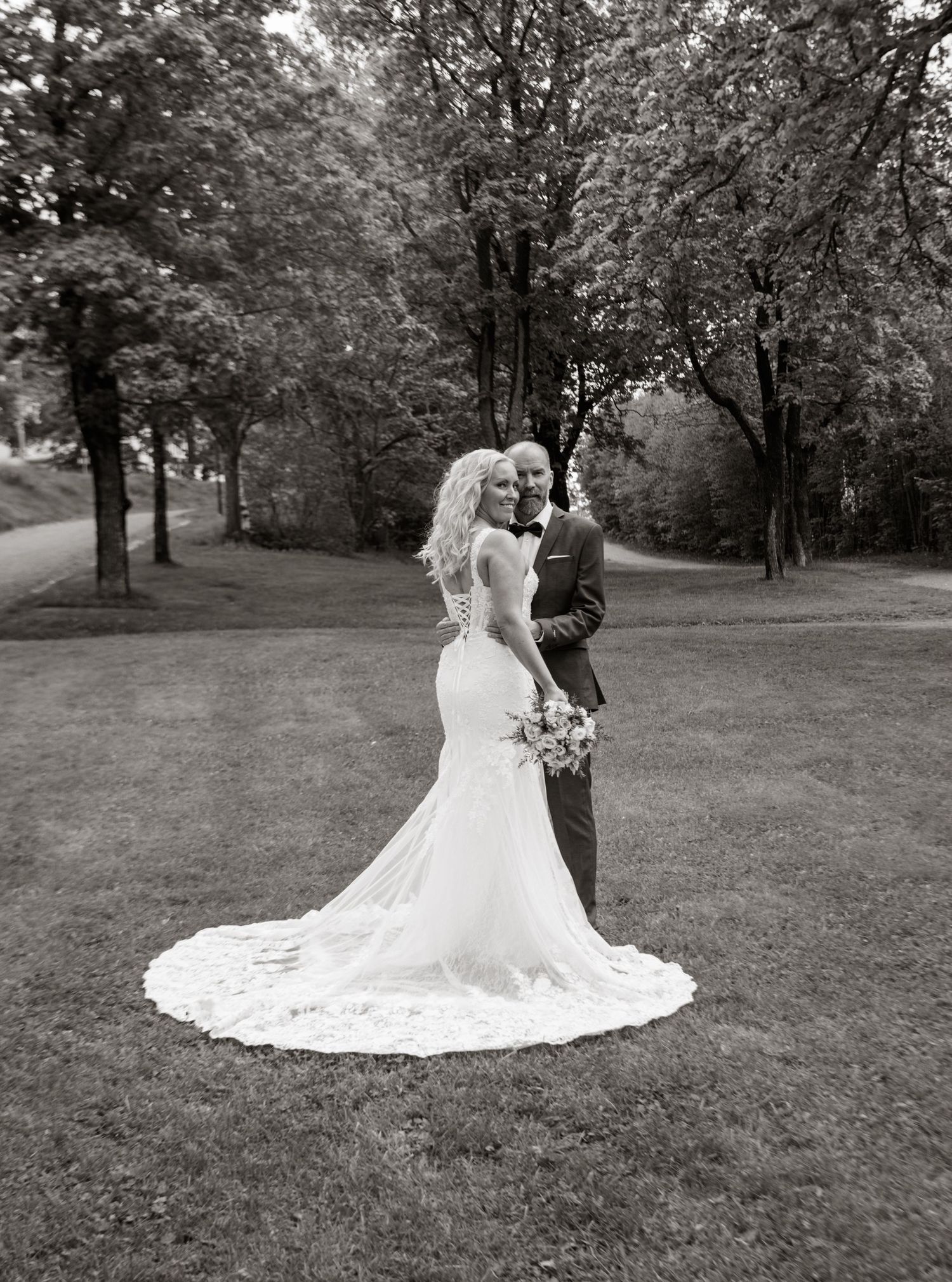 A black and white wedding portrait of a couple on a sweeping lawn with trailing bridal veil.