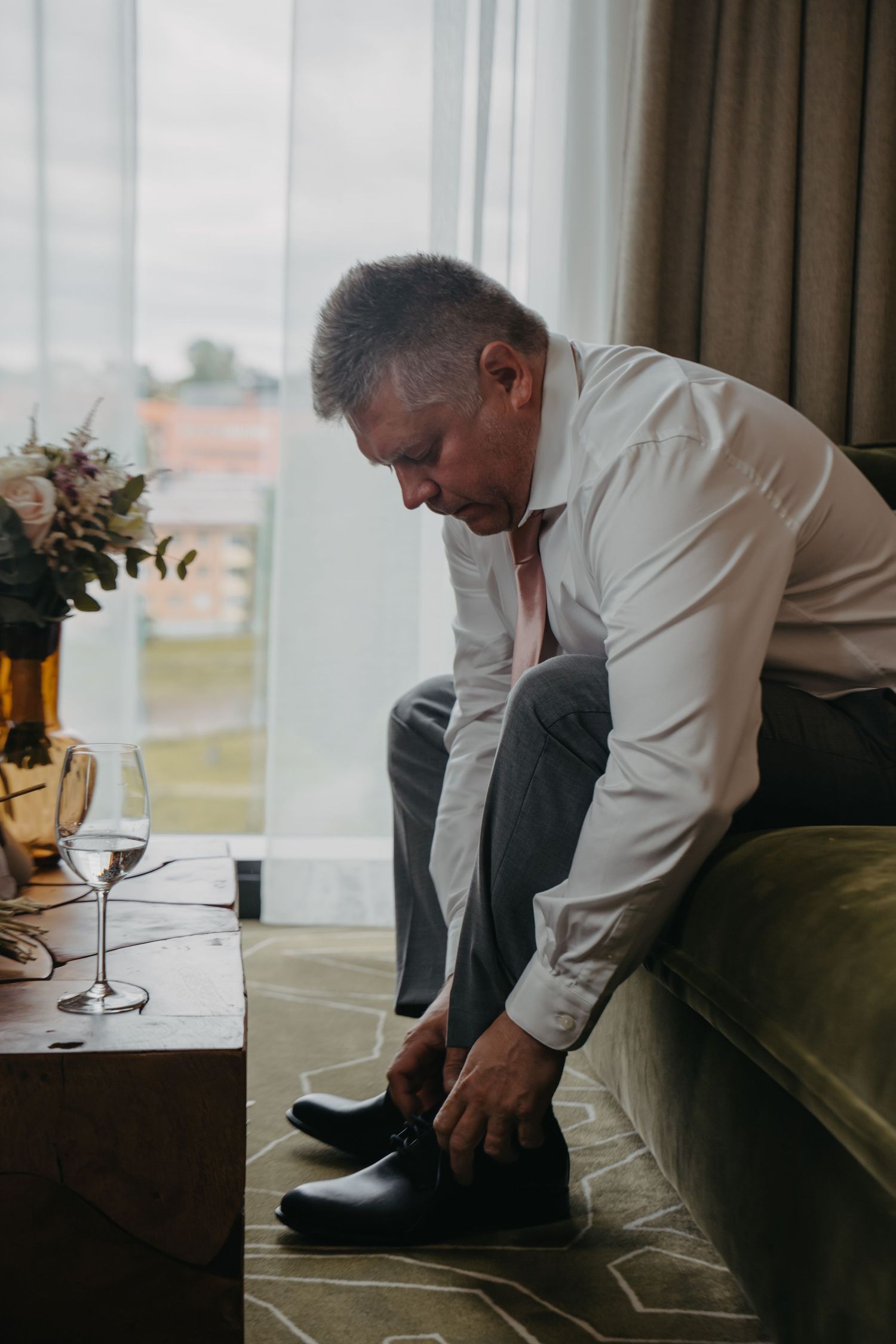 Person in white shirt putting on formal shoes while seated on green couch.