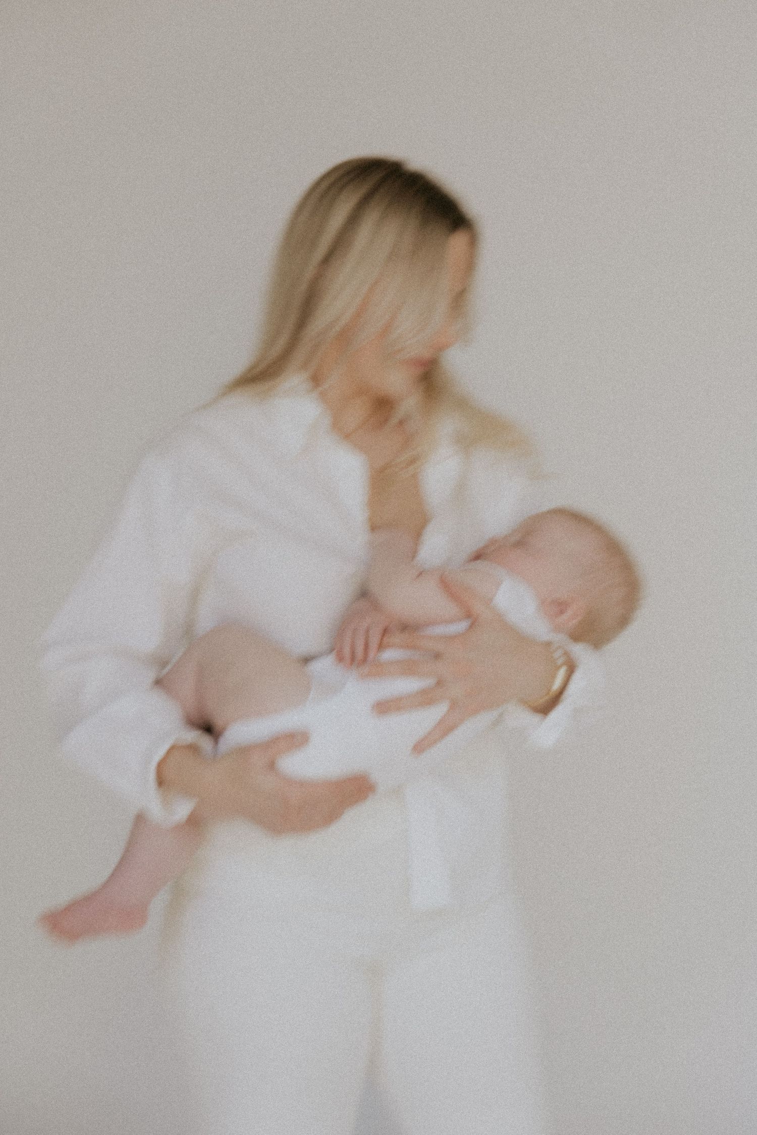 Ethereal portrait of mother in white holding infant in soft, dreamy lighting.