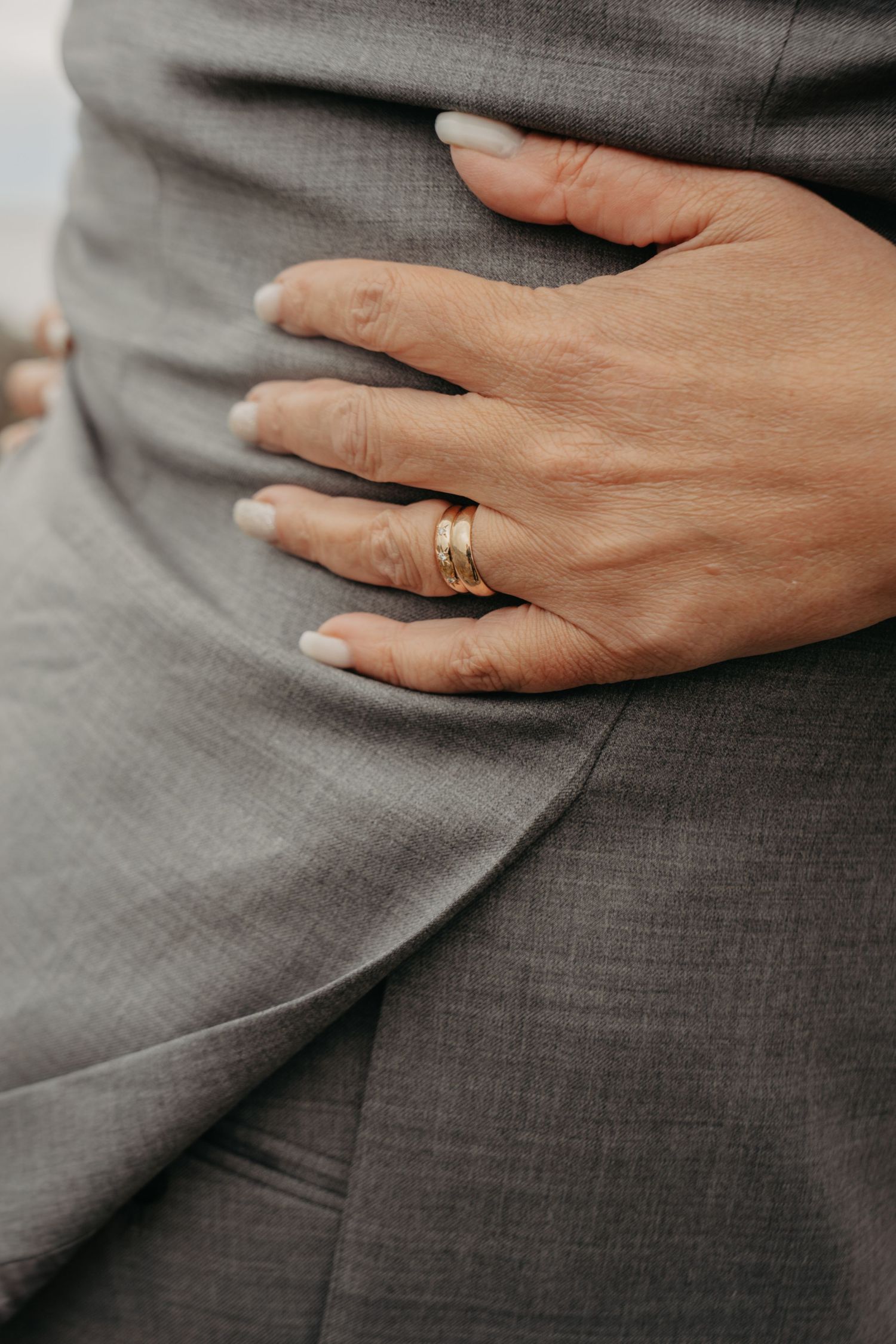 Close-up of a hand wearing gold wedding rings against gray fabric.