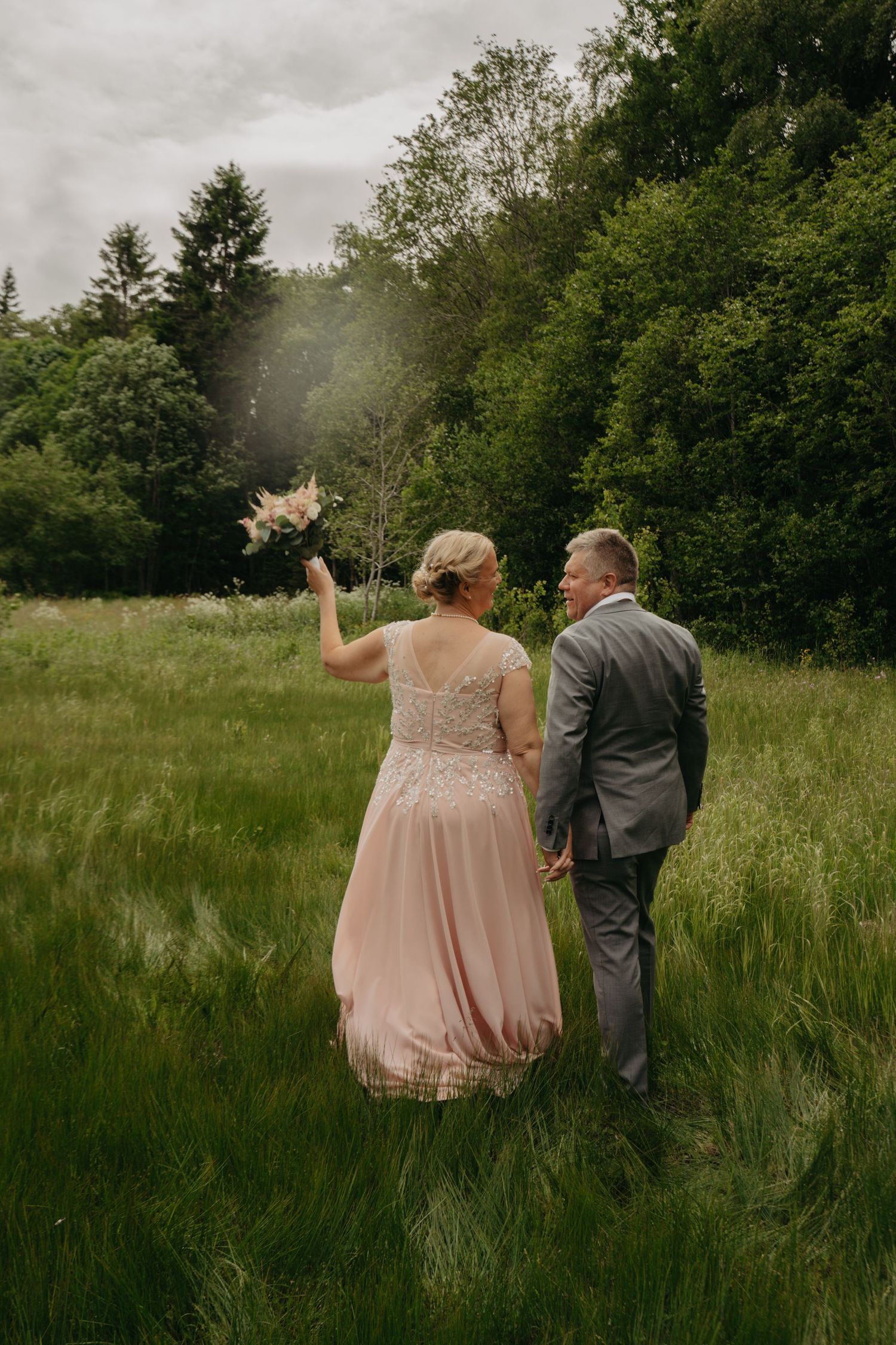 Wedding party walking through tall grass field on overcast day.