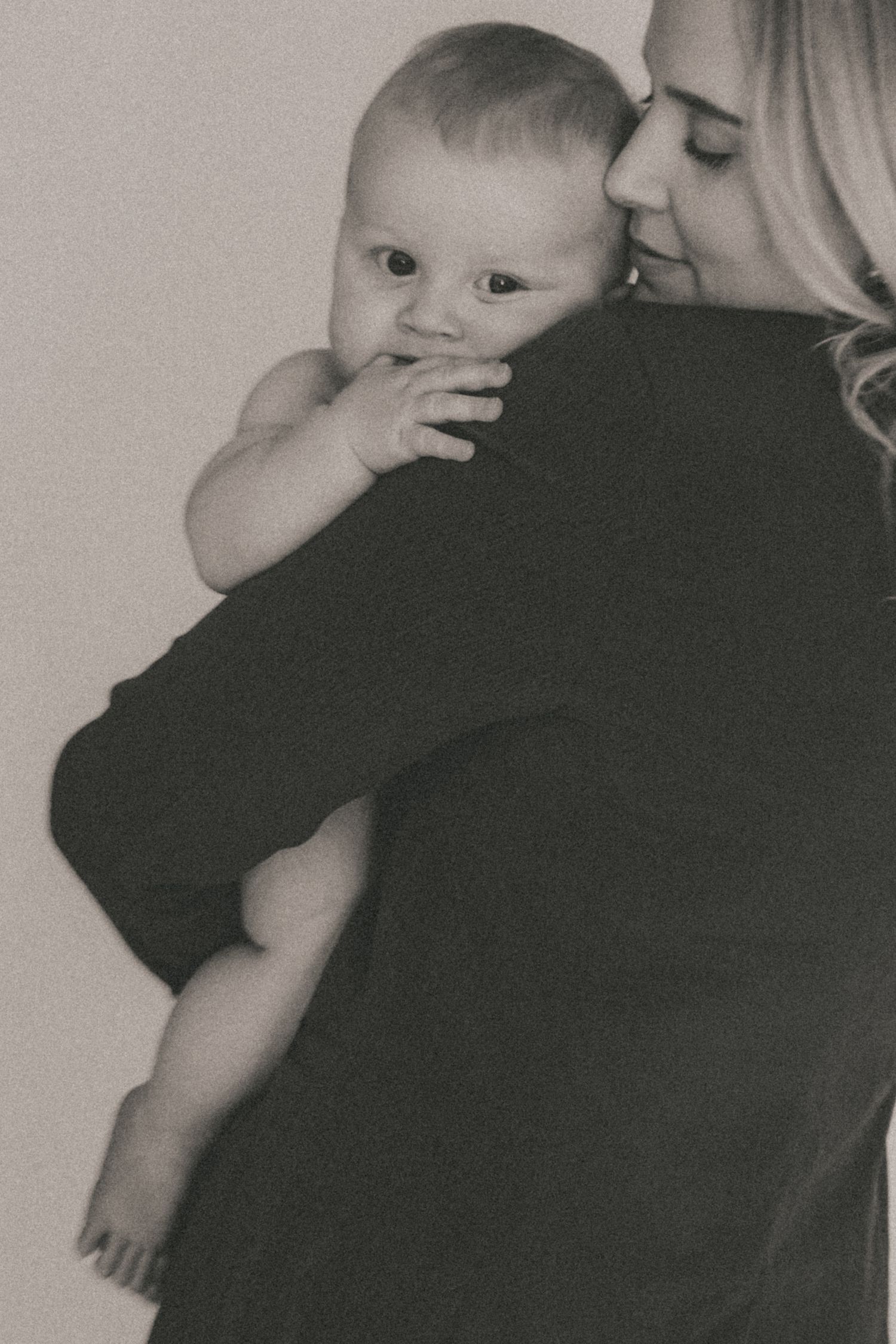 Black and white portrait of parent holding curious baby looking over shoulder.