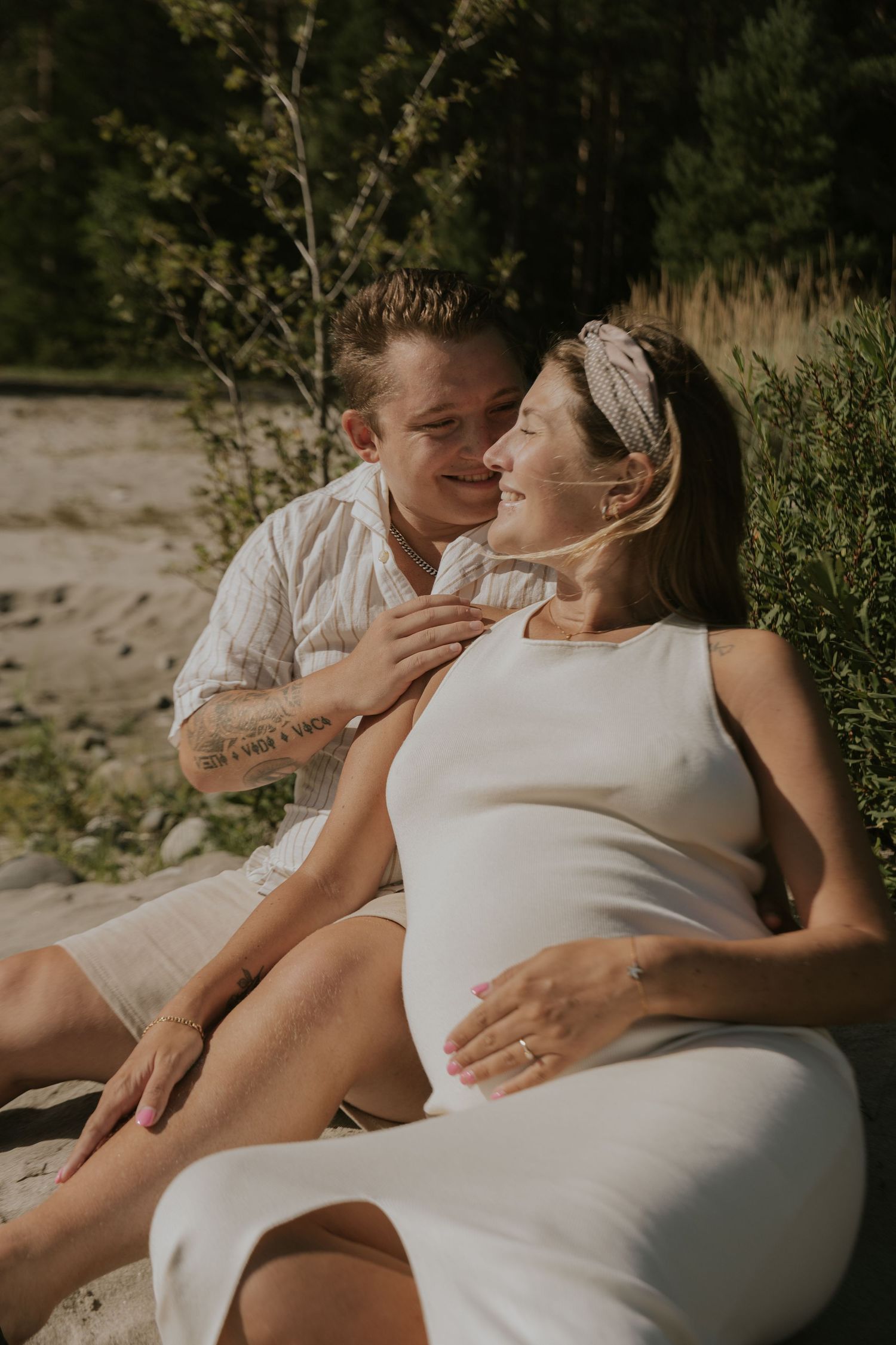 Intimate outdoor maternity photoshoot with couple lounging on blanket.