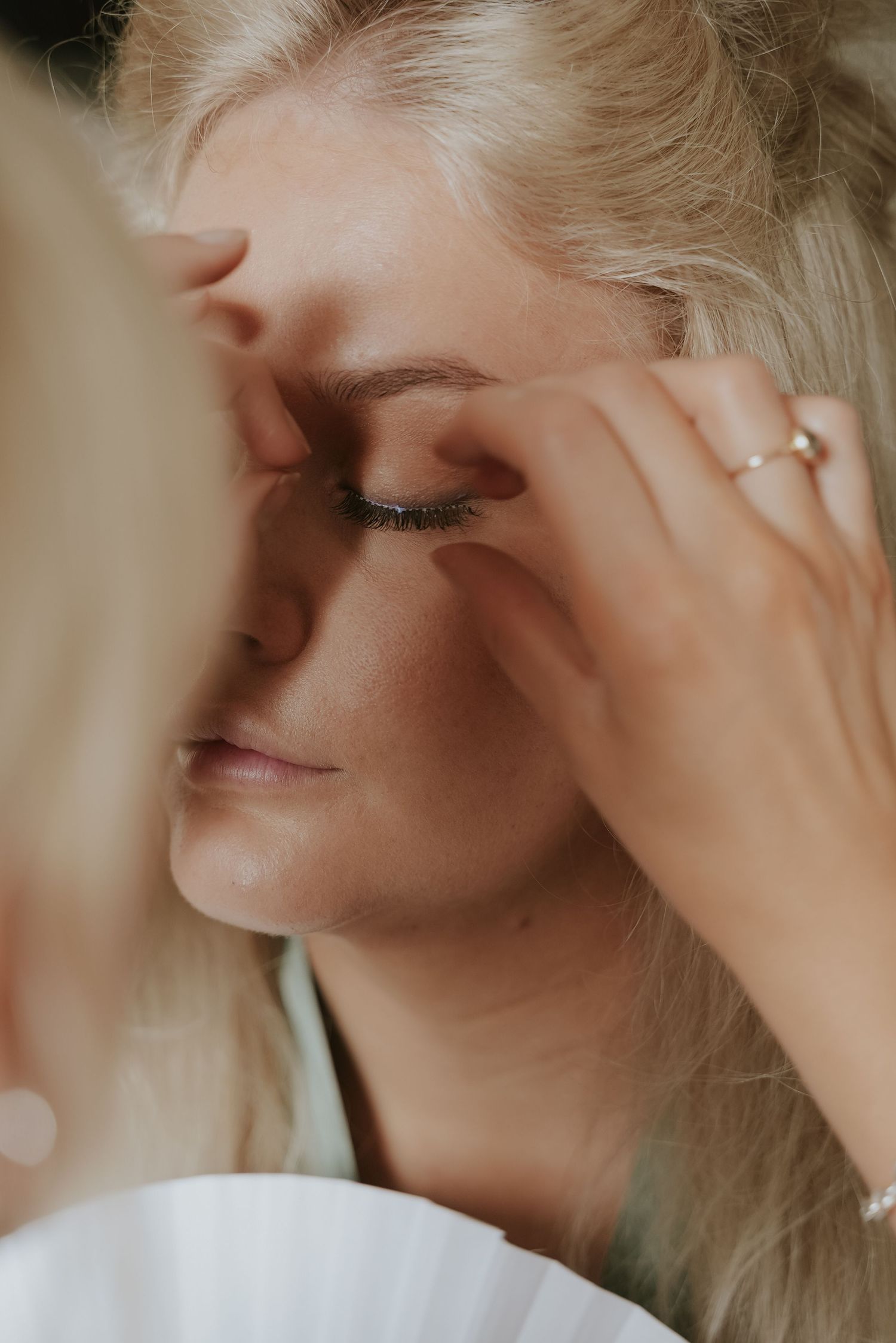 Close-up shot of someone having makeup applied to their eyes while wearing a white dress.