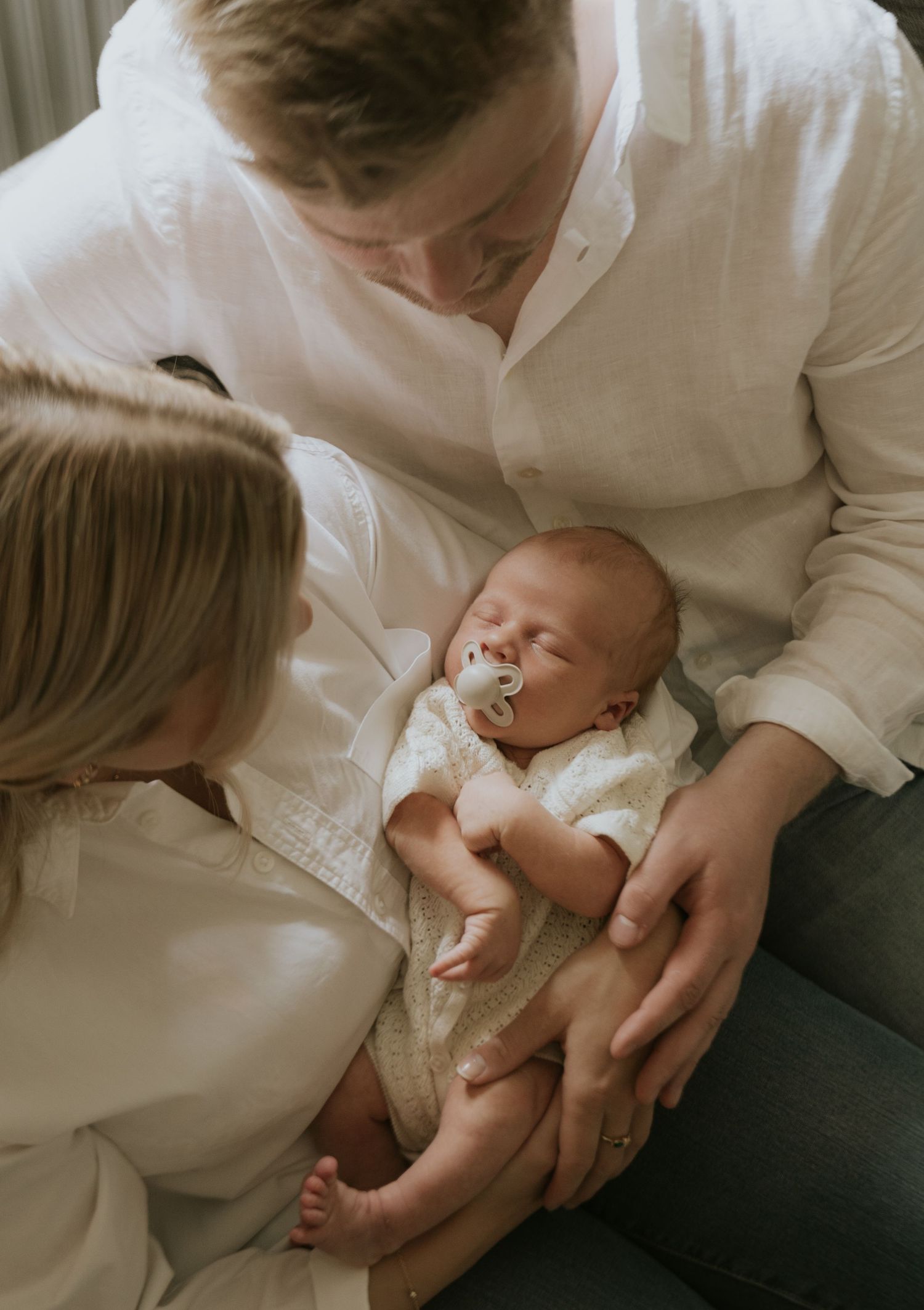 A series of tender moments between a parent and newborn baby wearing white clothing against a neutral background.