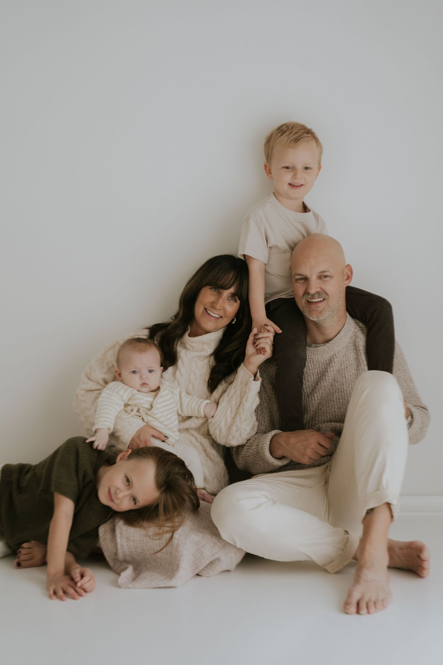 A family in neutral colored clothing lies together on a white floor in a minimalist photography series.