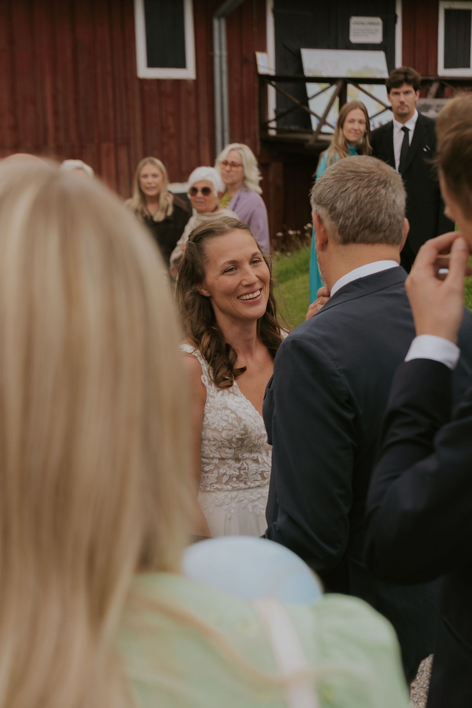 Wedding guests celebrate and gather outside a charming red barn on a sunny day.