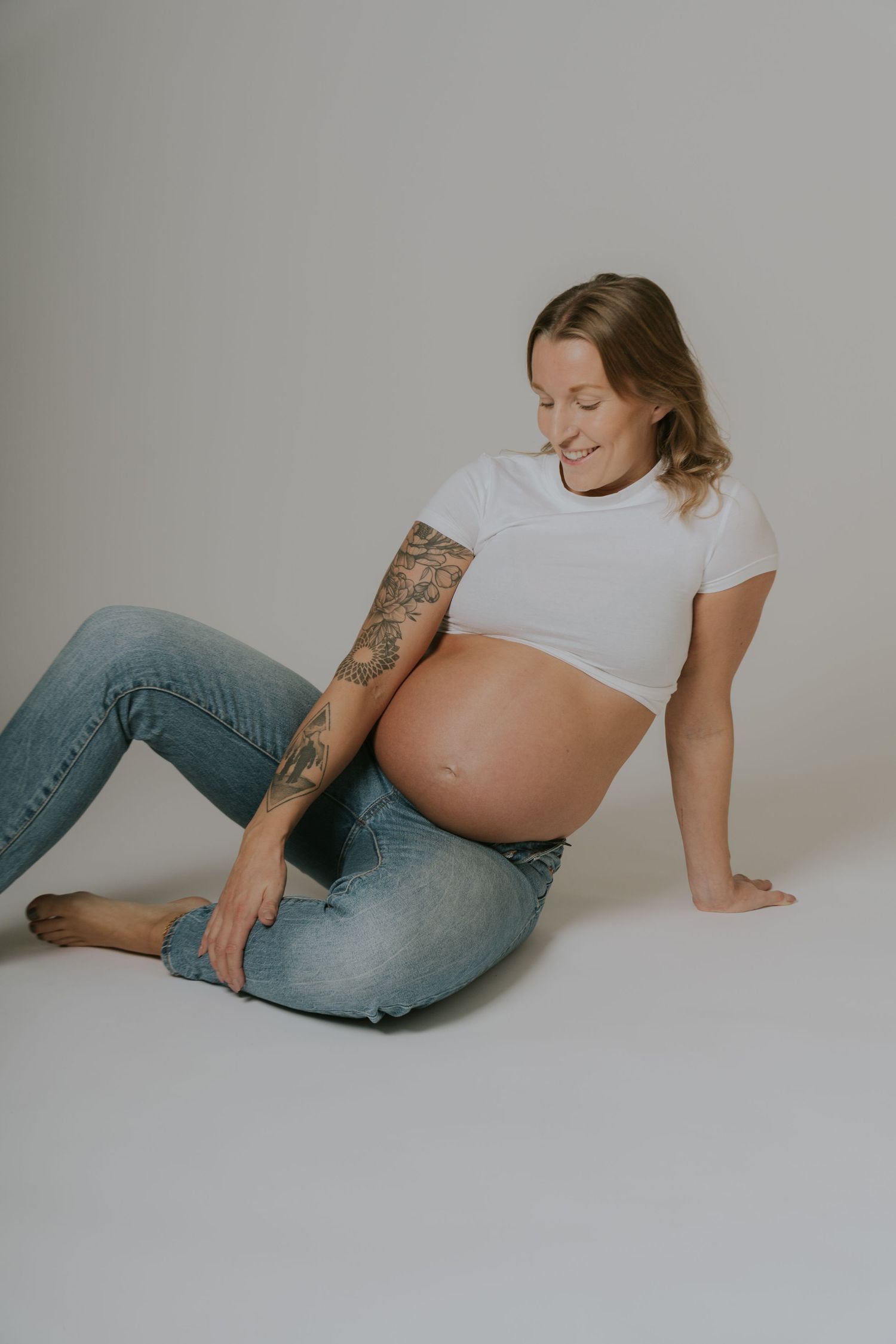 Casual maternity photos in jeans and white top showing relaxed poses on floor.