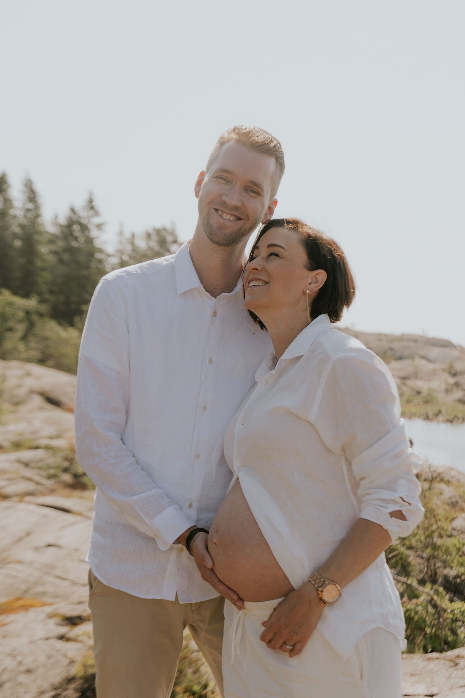 A couple in white clothing shares tender moments while posing together on a rocky outdoor setting during sunset.