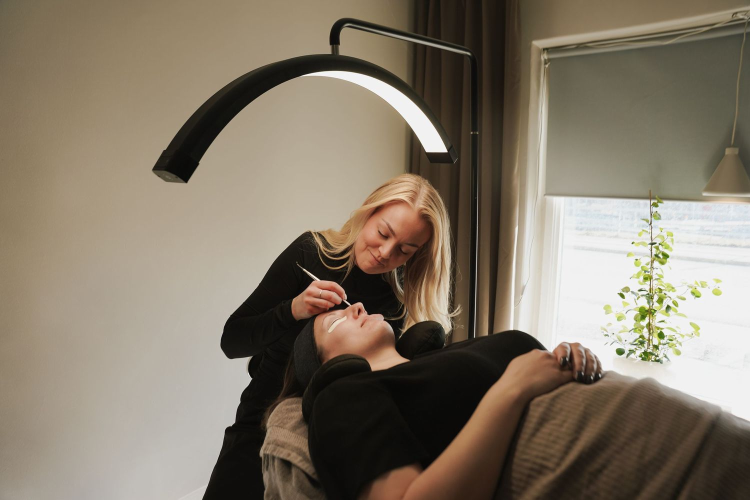 A person in black clothing lies on a couch in a sunlit room with minimalist decor.