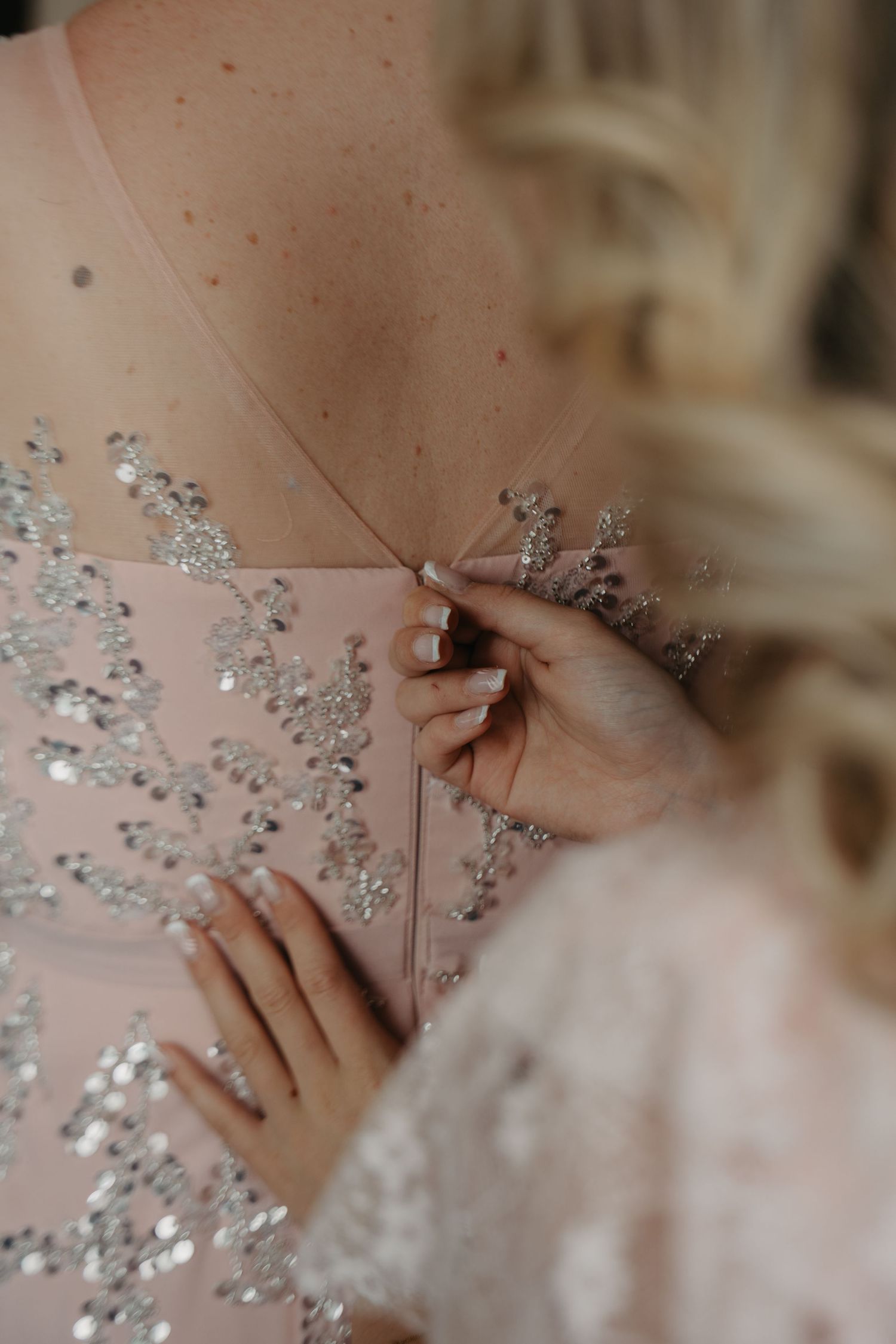 Close-up of hands fastening a sparkly embellished dress.