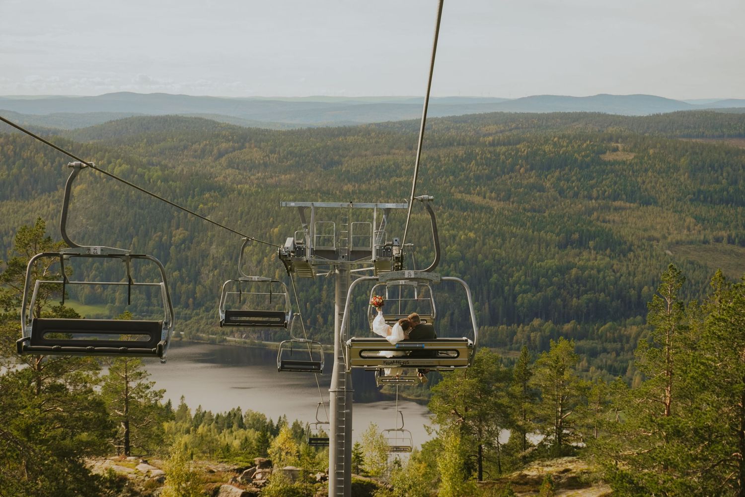 Ski lift chairs ascending mountain with scenic forest vista below.