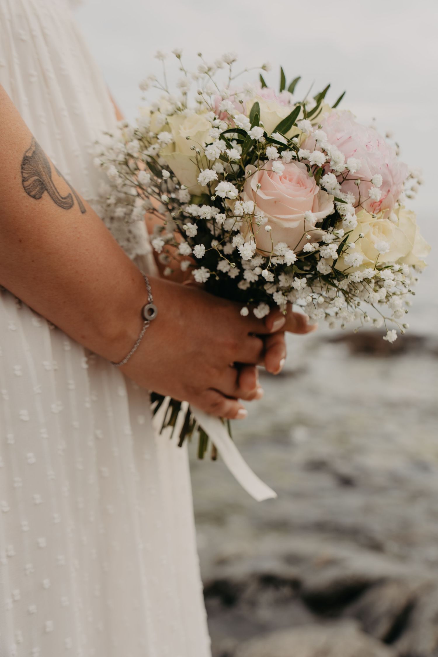 Delicate bridal bouquet with pink roses and baby's breath against coastal background.