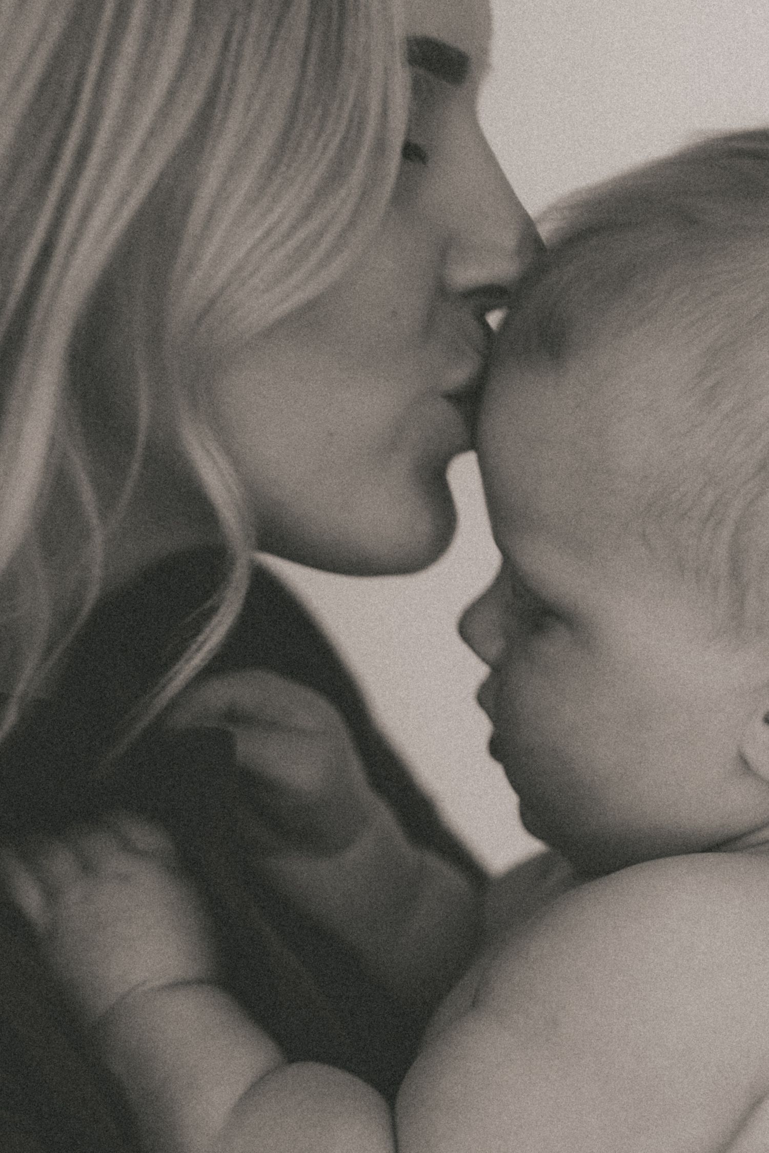 Black and white intimate close-up of parent giving baby a gentle kiss.