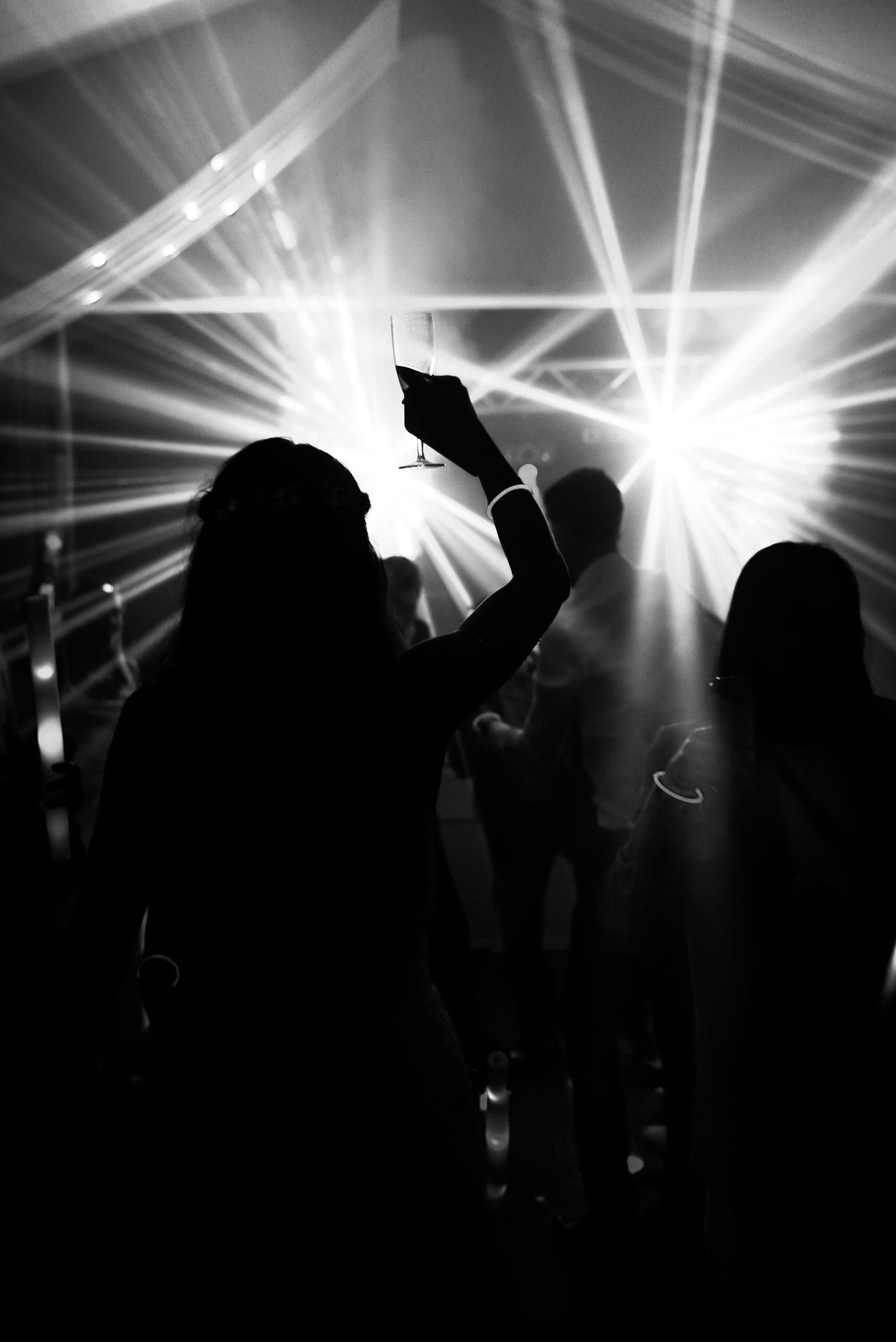 Silhouettes of people dancing at a nightclub with bright white spotlights and beams illuminating the dark atmosphere.