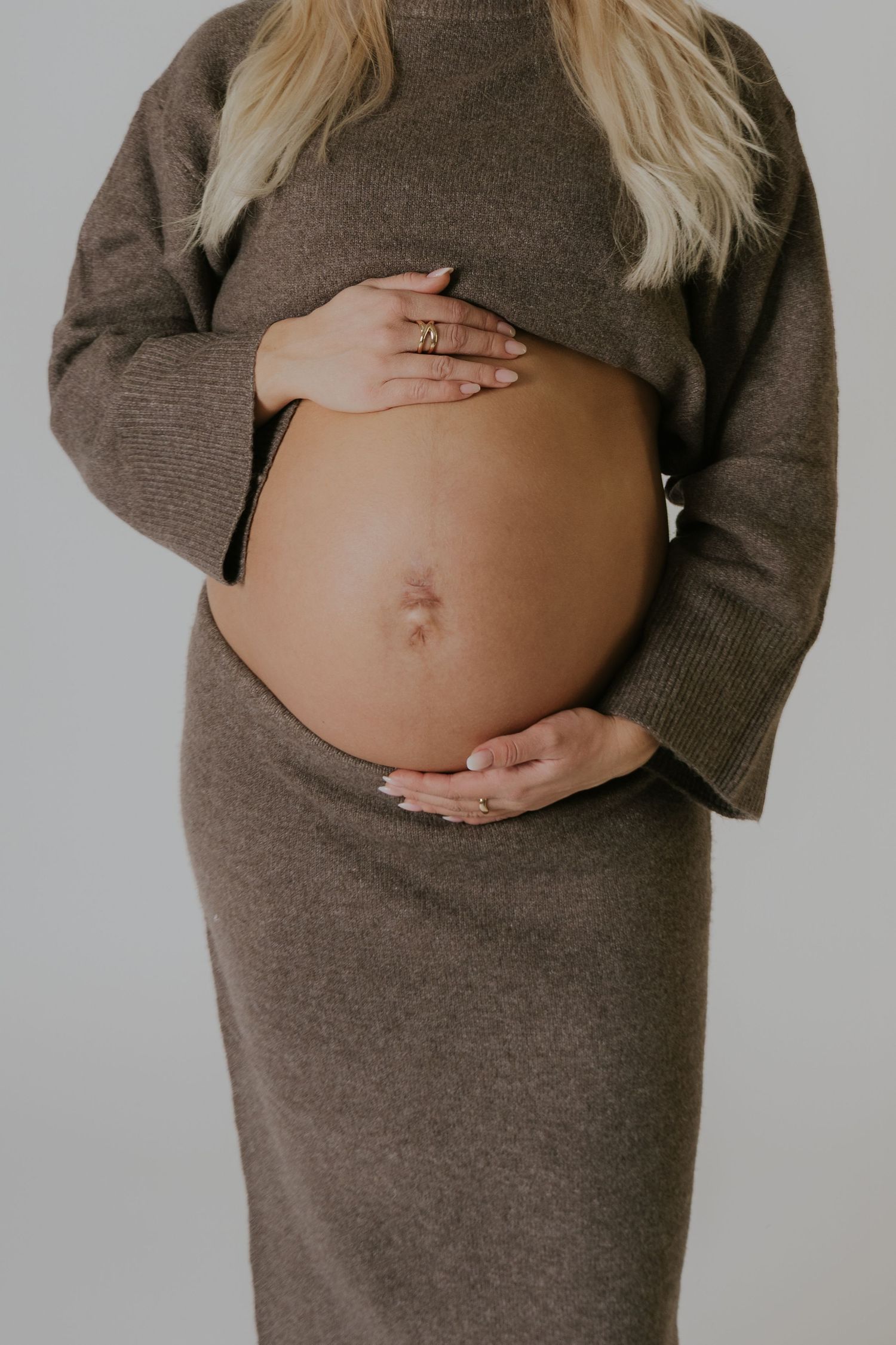 A series of artistic maternity photos showing a pregnant belly in a brown sweater against a neutral background.
