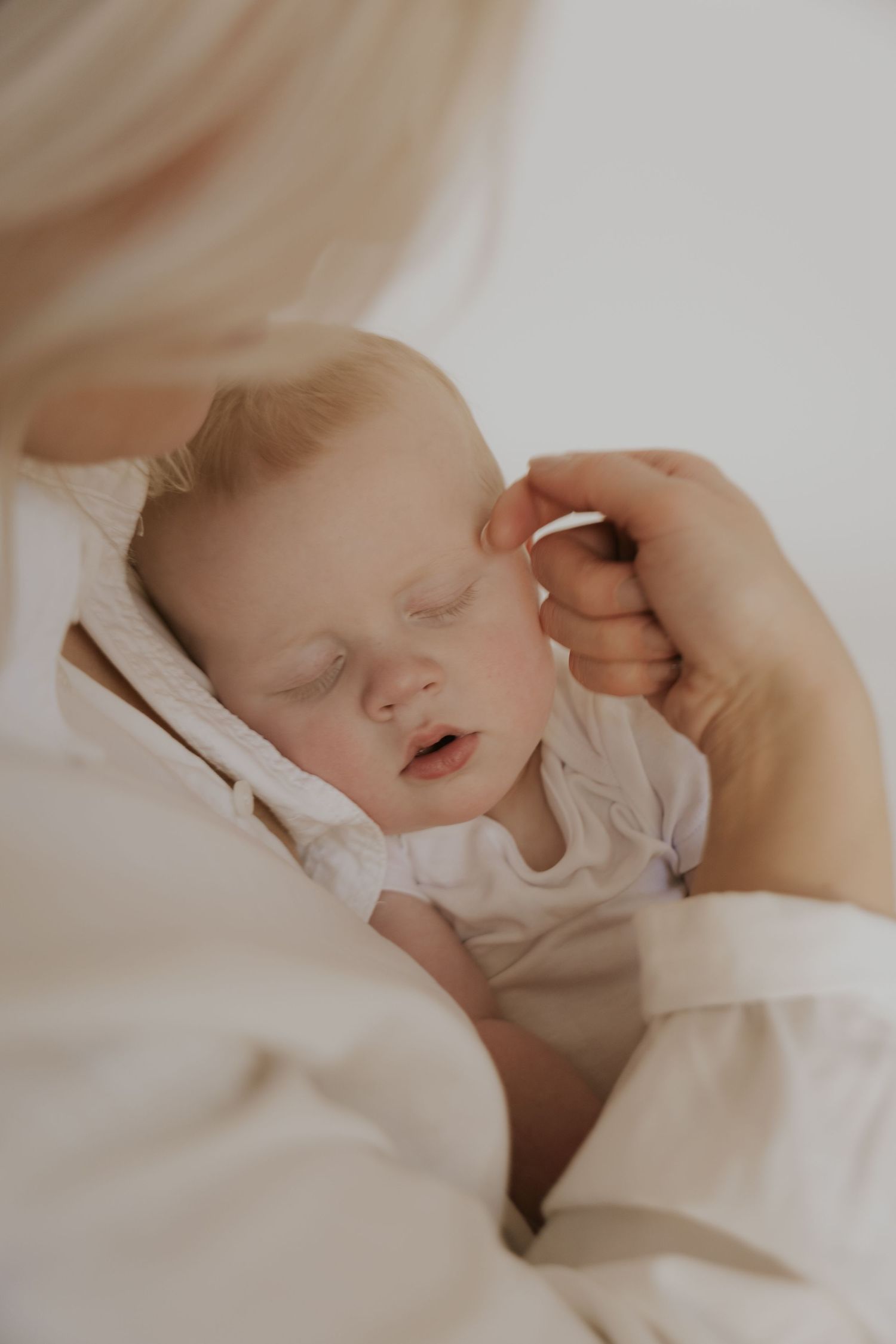 Close-up of a sleeping baby in soft white bedding.