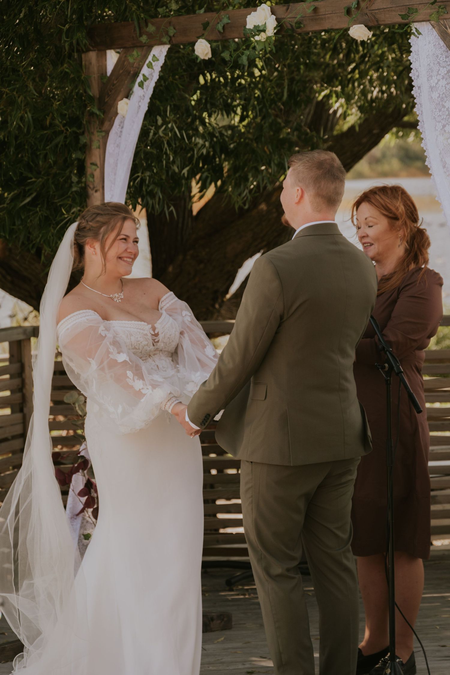 Intimate outdoor wedding ceremony with couple exchanging vows under a wooden pergola.