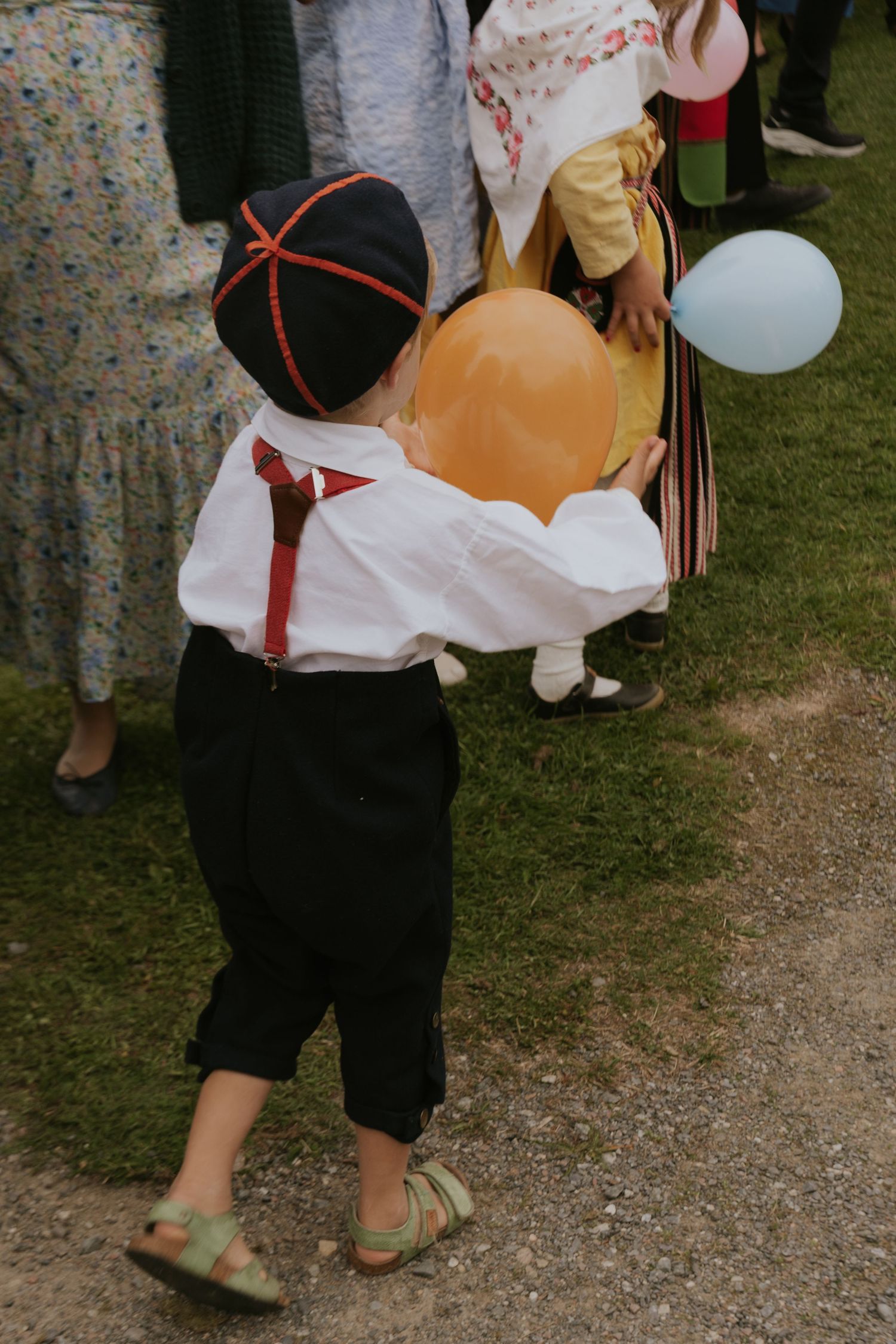 People in traditional German folk costumes walk together on a gravel path during a festival celebration.