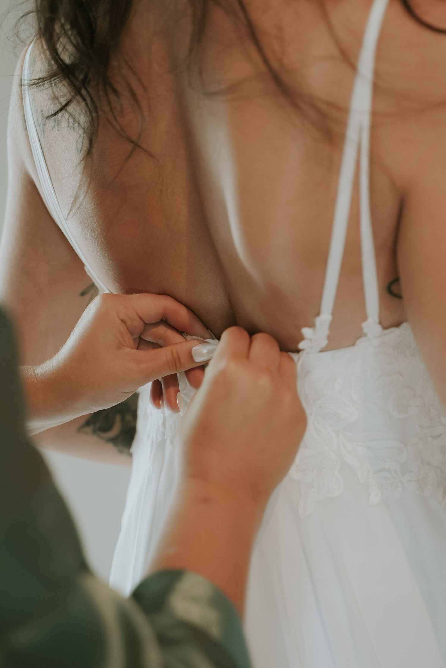 Artistic detail shot of white bridal gown straps and lace trim against a soft neutral background.