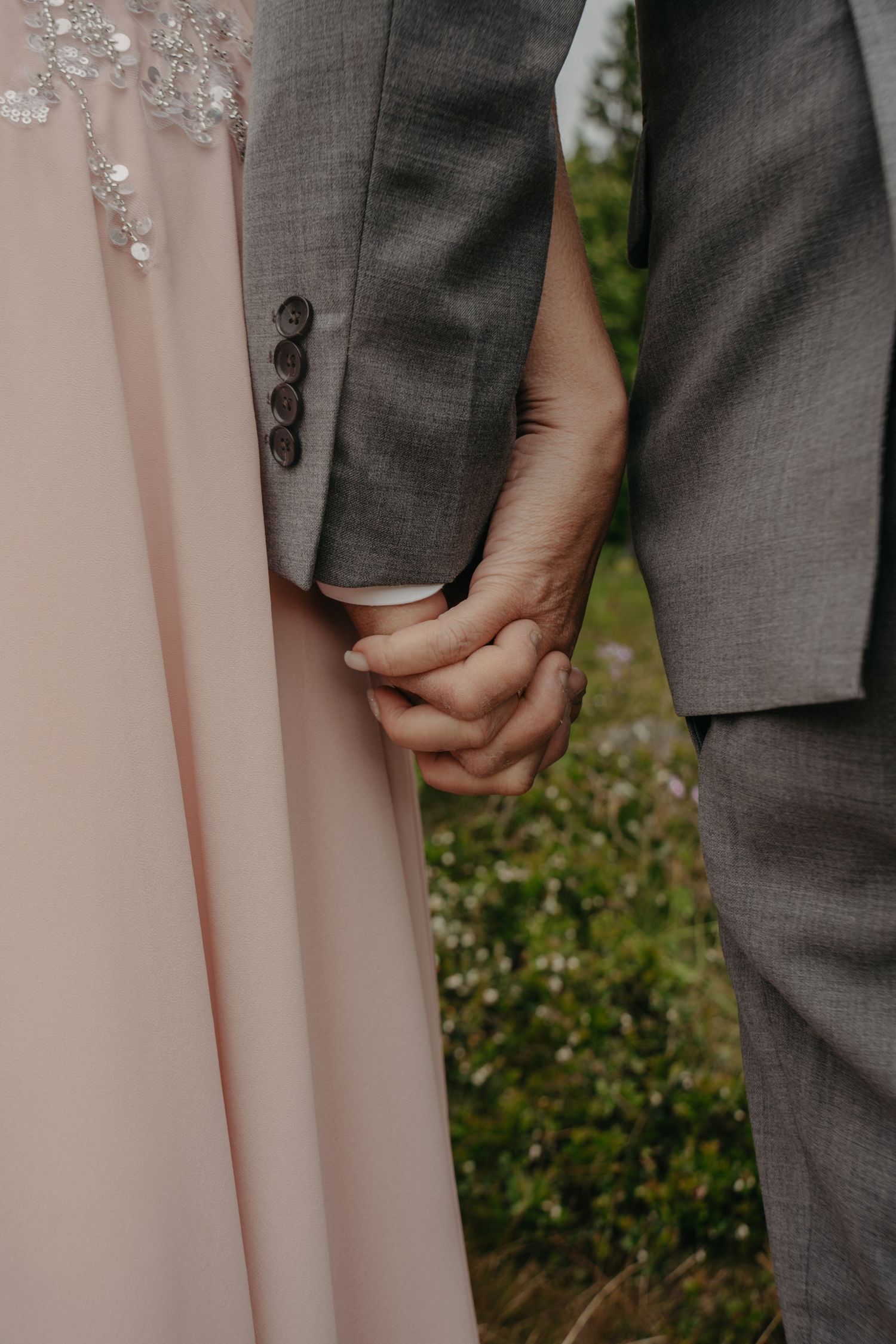 Close-up of clasped hands showing the contrast between gray suit and pink dress fabric.