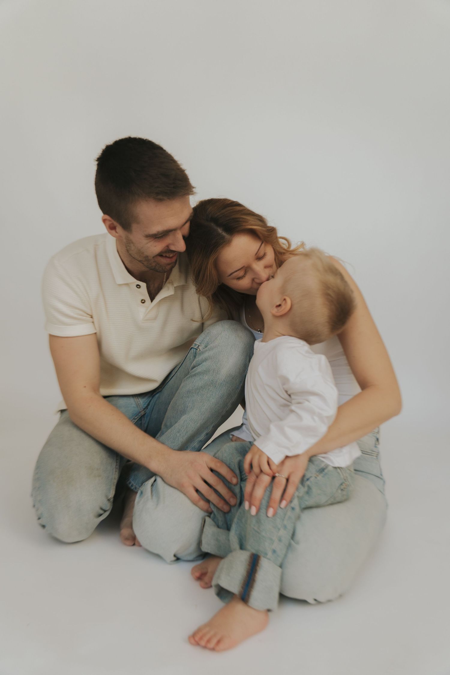 A couple in casual white and gray outfits share tender moments while sitting together on a light background.