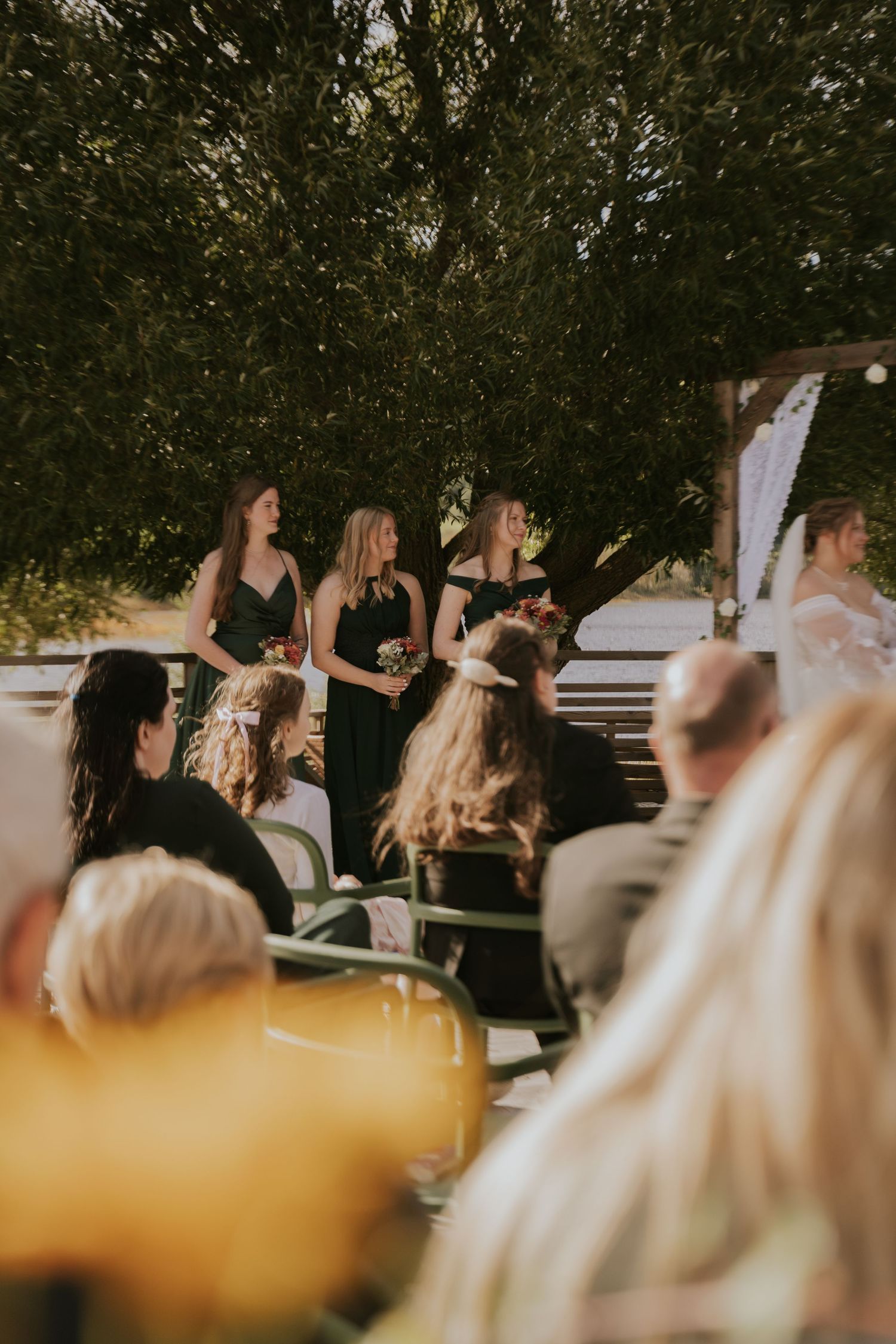 Wedding guests watch ceremony from seats during golden hour outdoors.