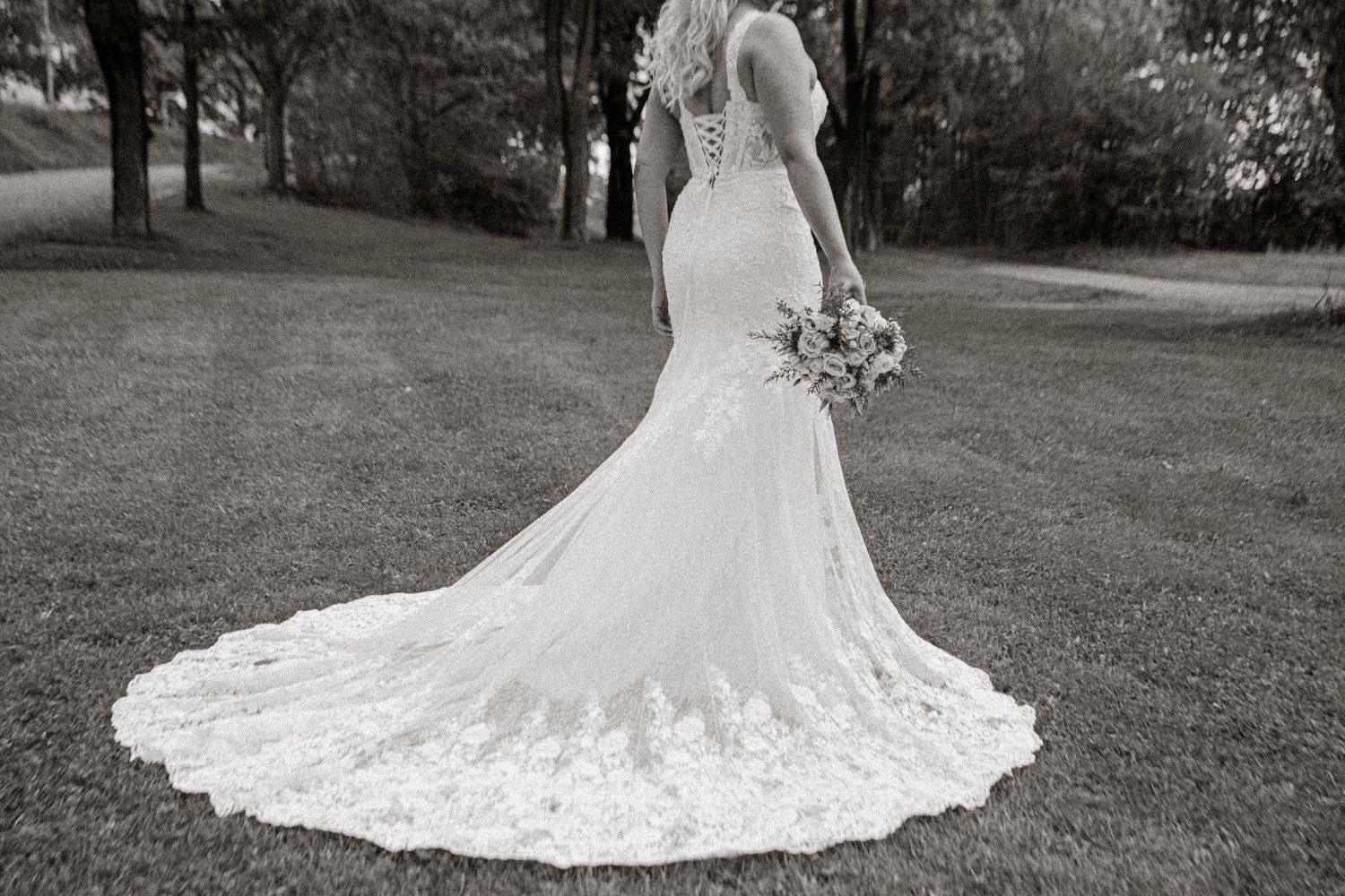 Detailed view of an ornate lace wedding dress train spread out on grass.