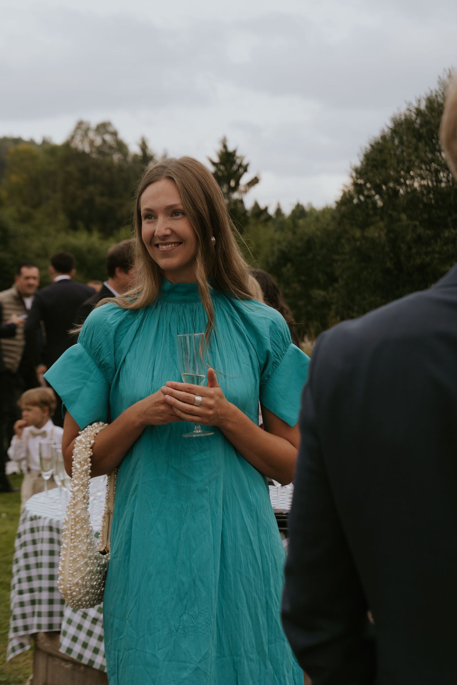 Wedding guests in turquoise dress enjoying outdoor celebration with drinks and laughter.