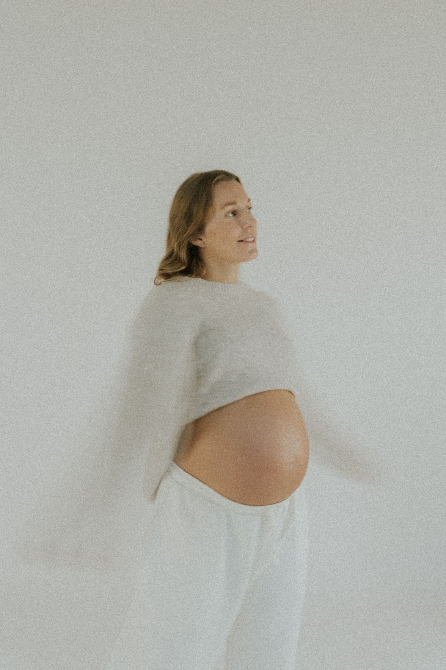 Artistic maternity photos showing an expectant mother in a flowing white dress against a light background.