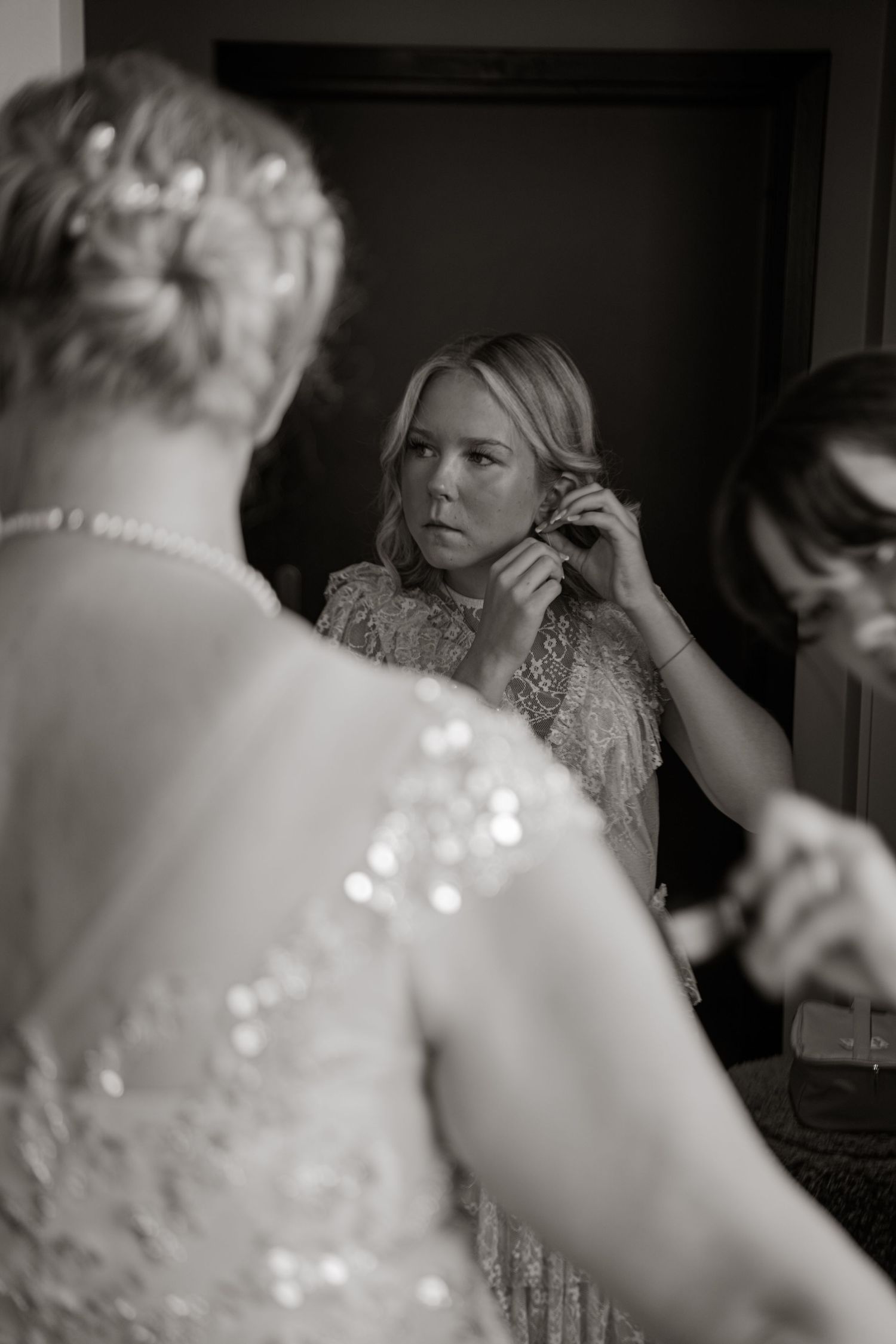 Black and white photos showing the process of putting on earrings in a mirror.