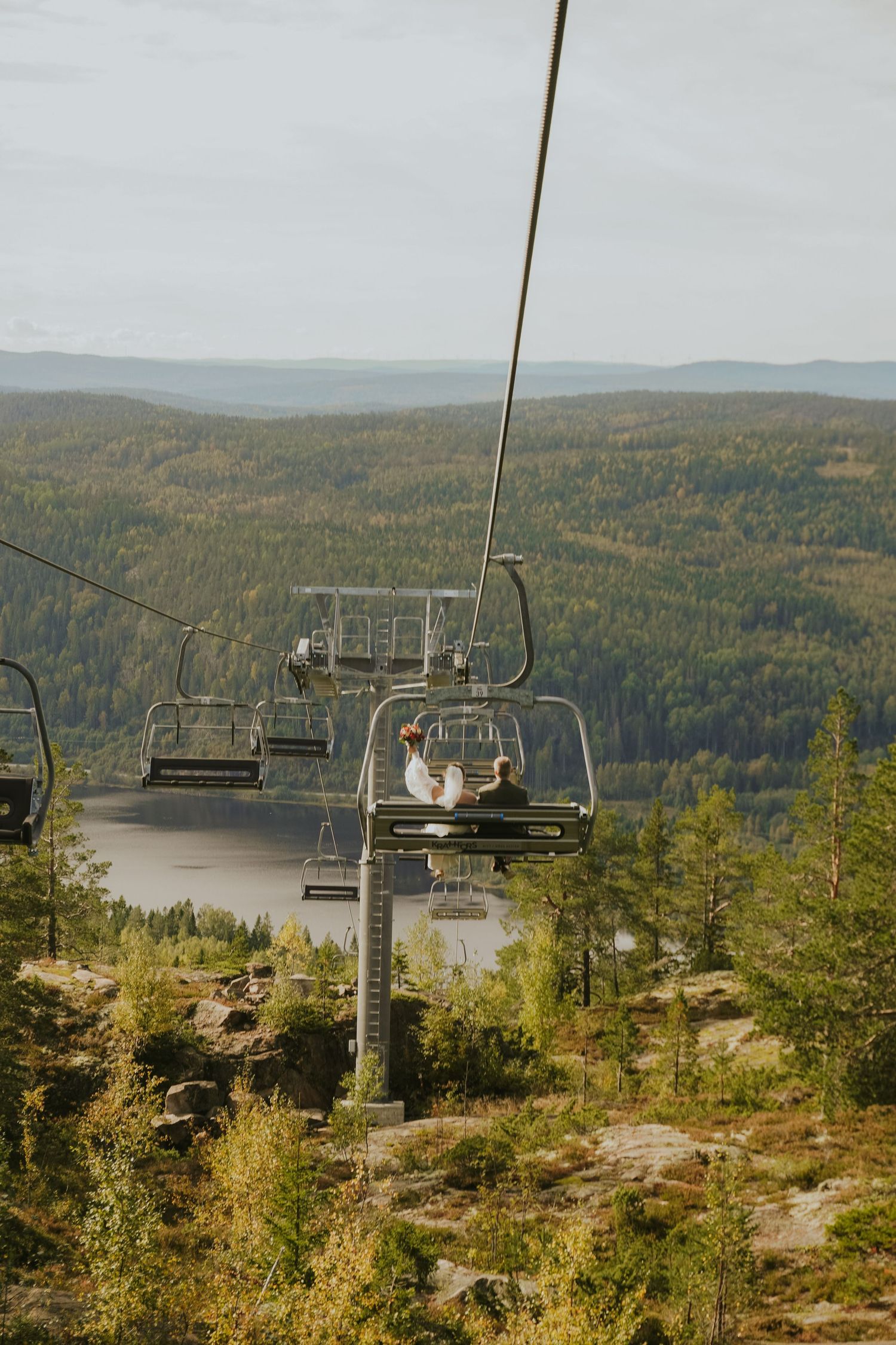 Ski lift chairs traverse a mountain landscape with autumn foliage and a lake below.