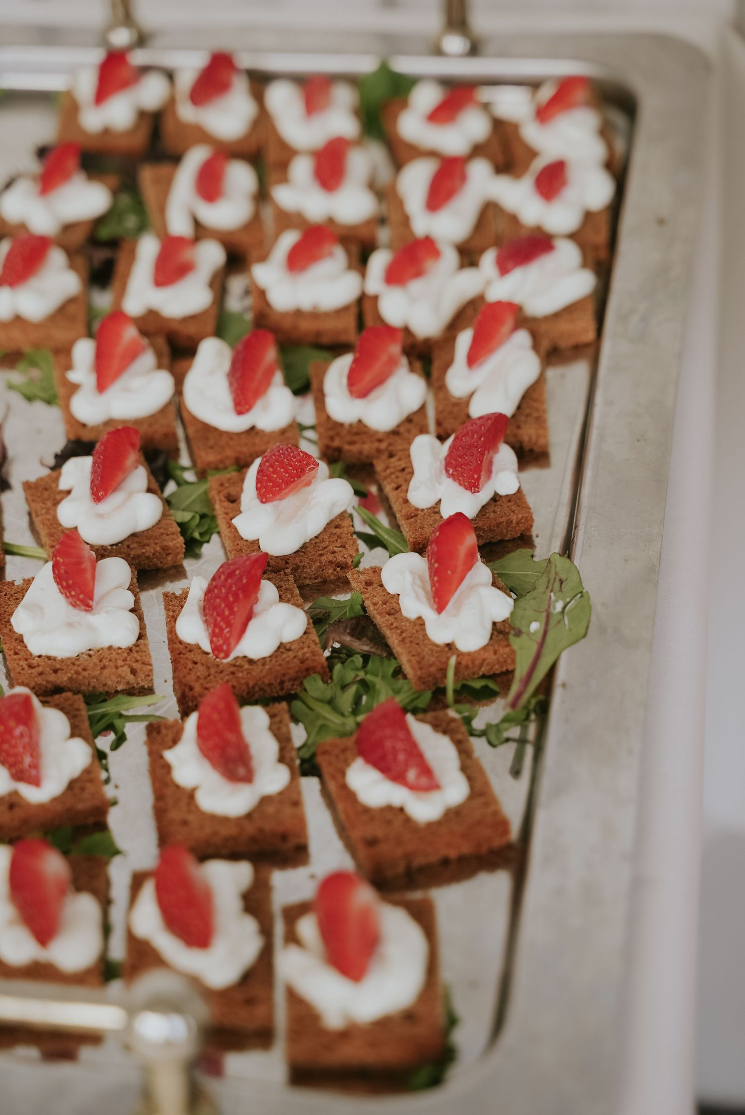 Appetizer bites made with toast points topped with whipped cream and fresh strawberries arranged on a serving platter.
