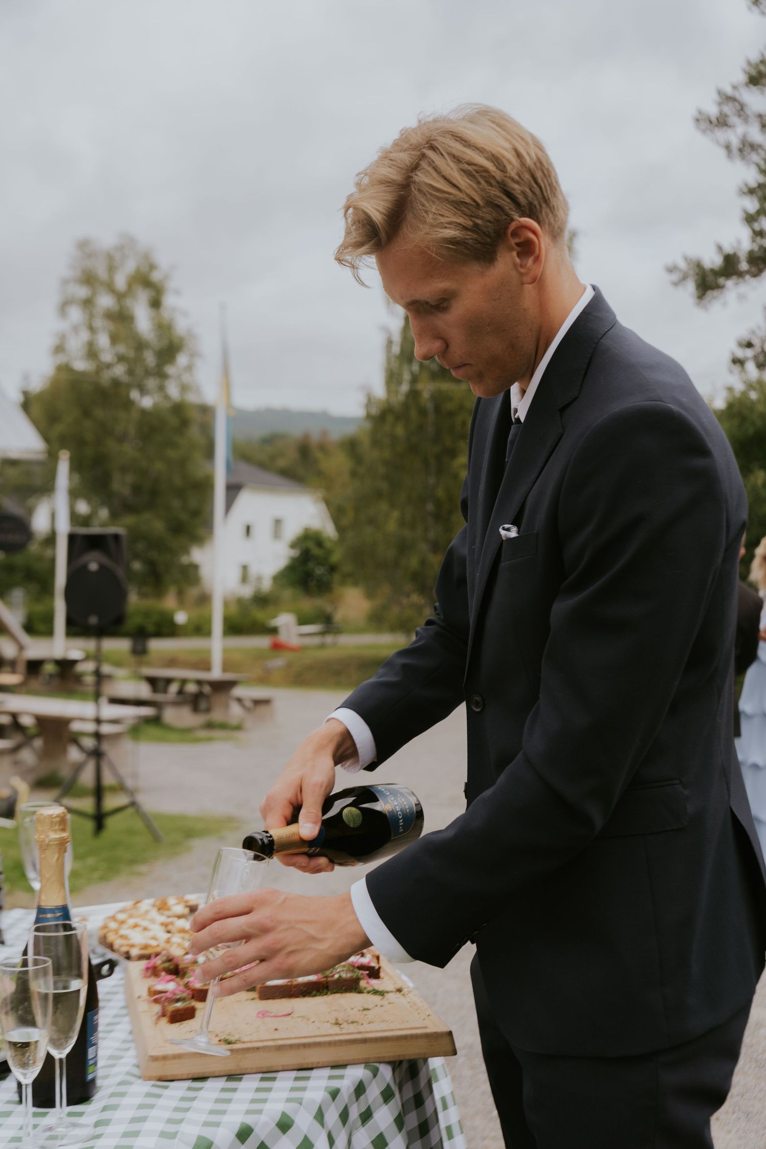 Person in formal attire arranging appetizers on wooden boards at an outdoor event.