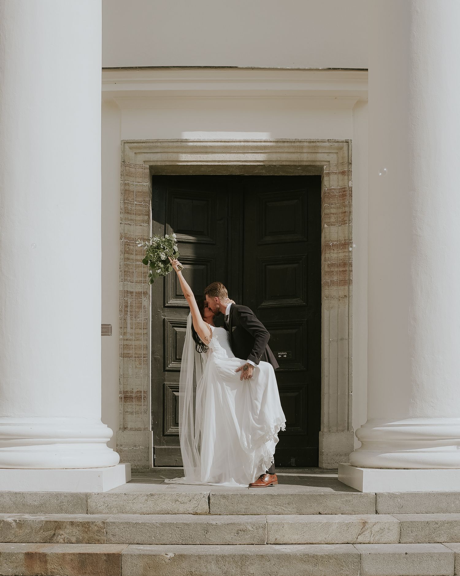 Artistic wedding portrait on white stone steps with classical architecture.