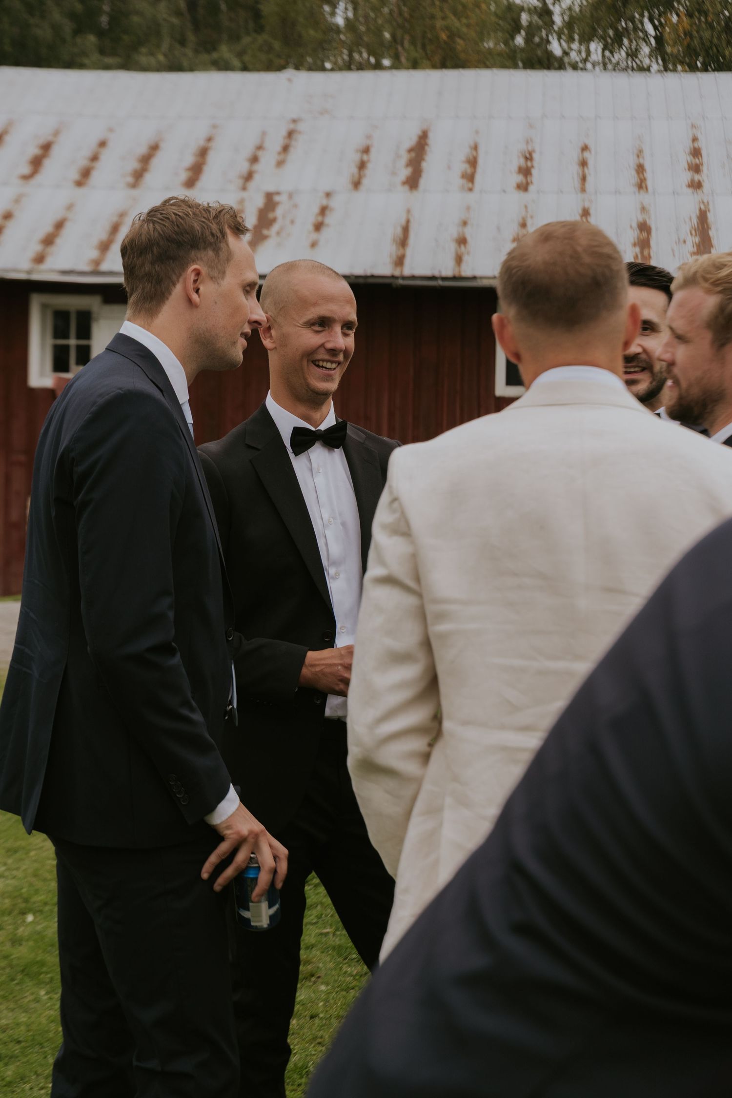 Groomsmen in black tuxedos share laughs during outdoor wedding celebration.
