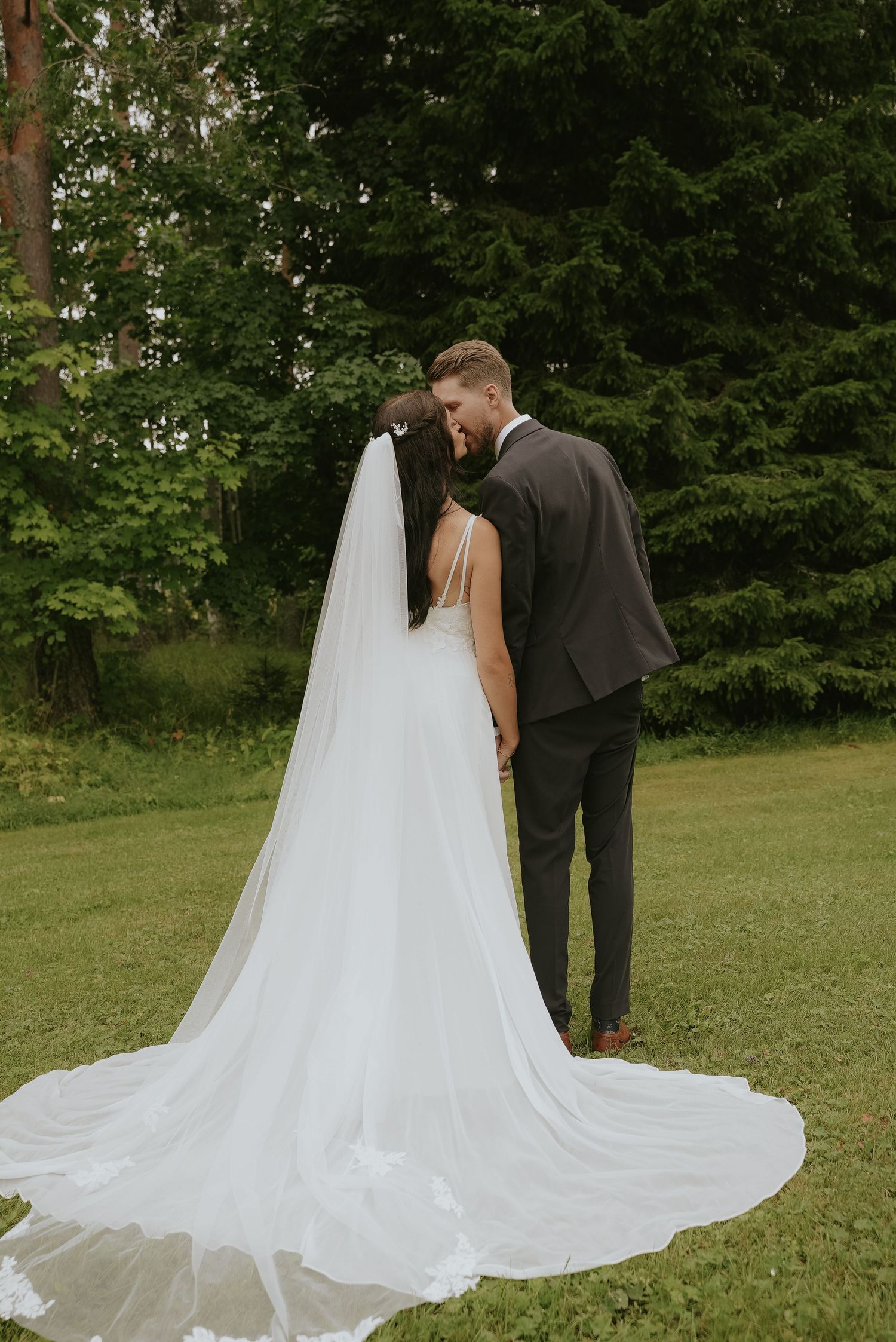 A bride and groom share a romantic moment in a lush green garden setting with a flowing cathedral-length veil.
