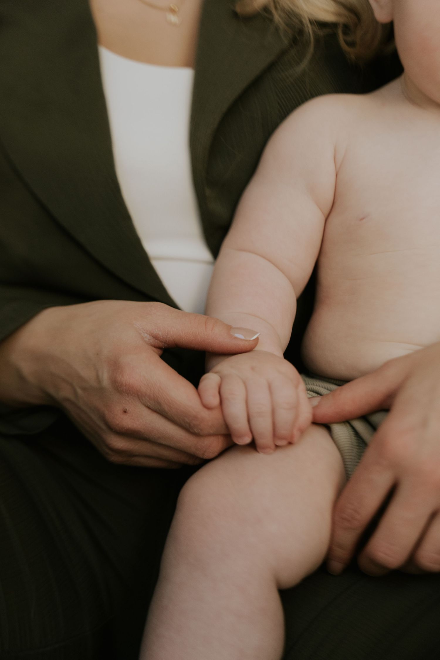 Close-up of gentle hands holding a baby's tiny fingers against dark fabric.