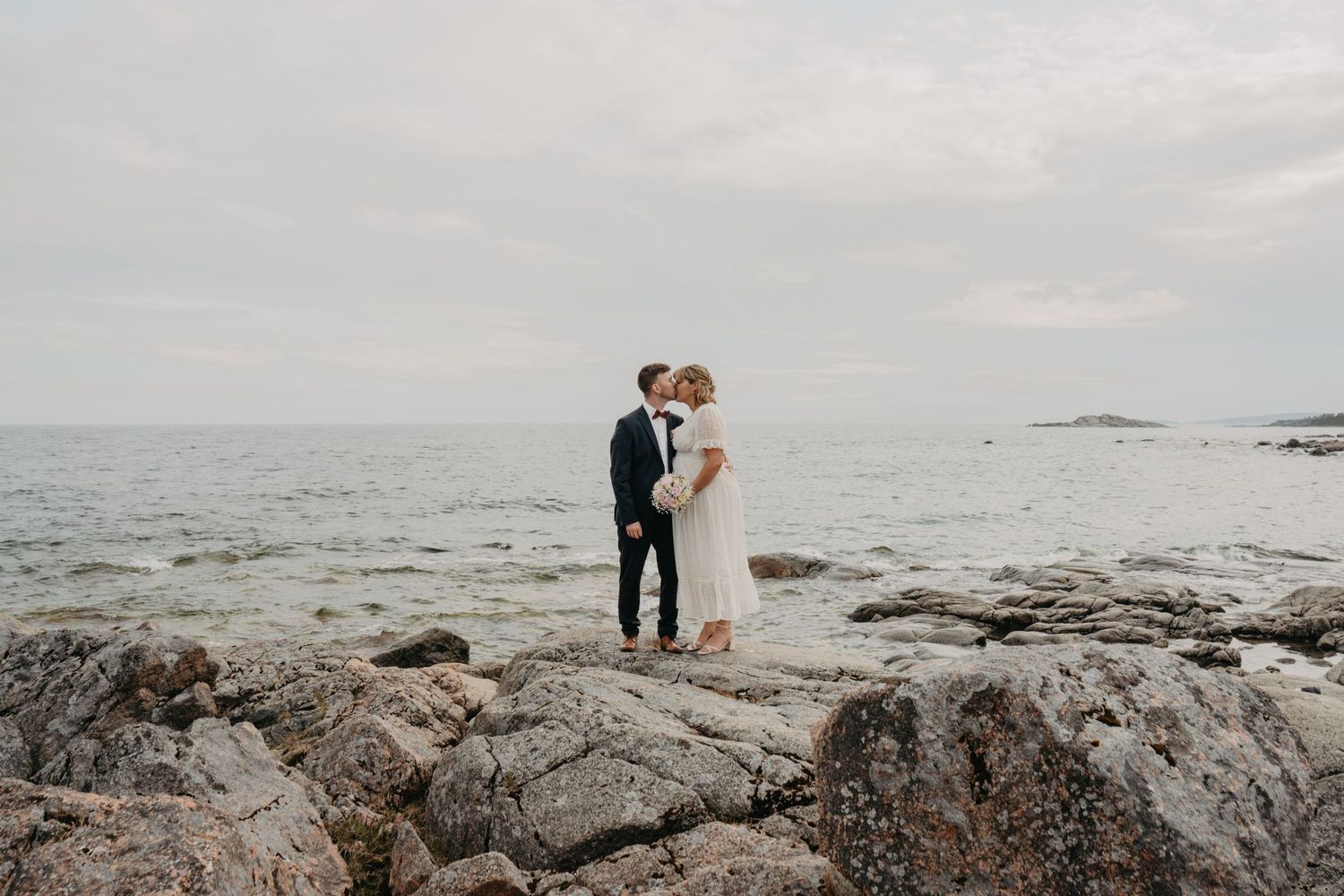 Wedding couple embracing on rocky coastal cliffs with ocean views.