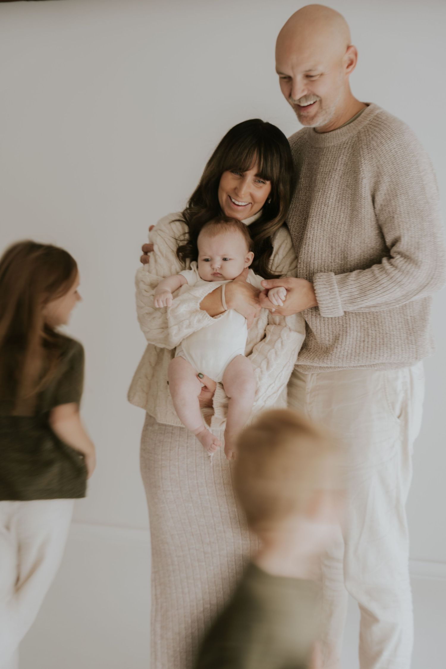 A joyful family portrait with a baby in matching neutral-toned outfits.