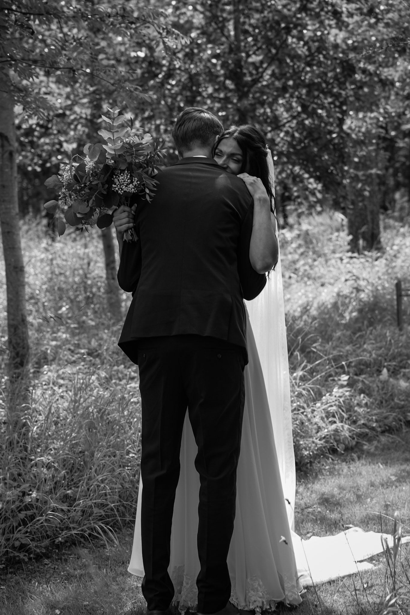 A black and white wedding portrait of a couple sharing an intimate moment in a wooded setting.