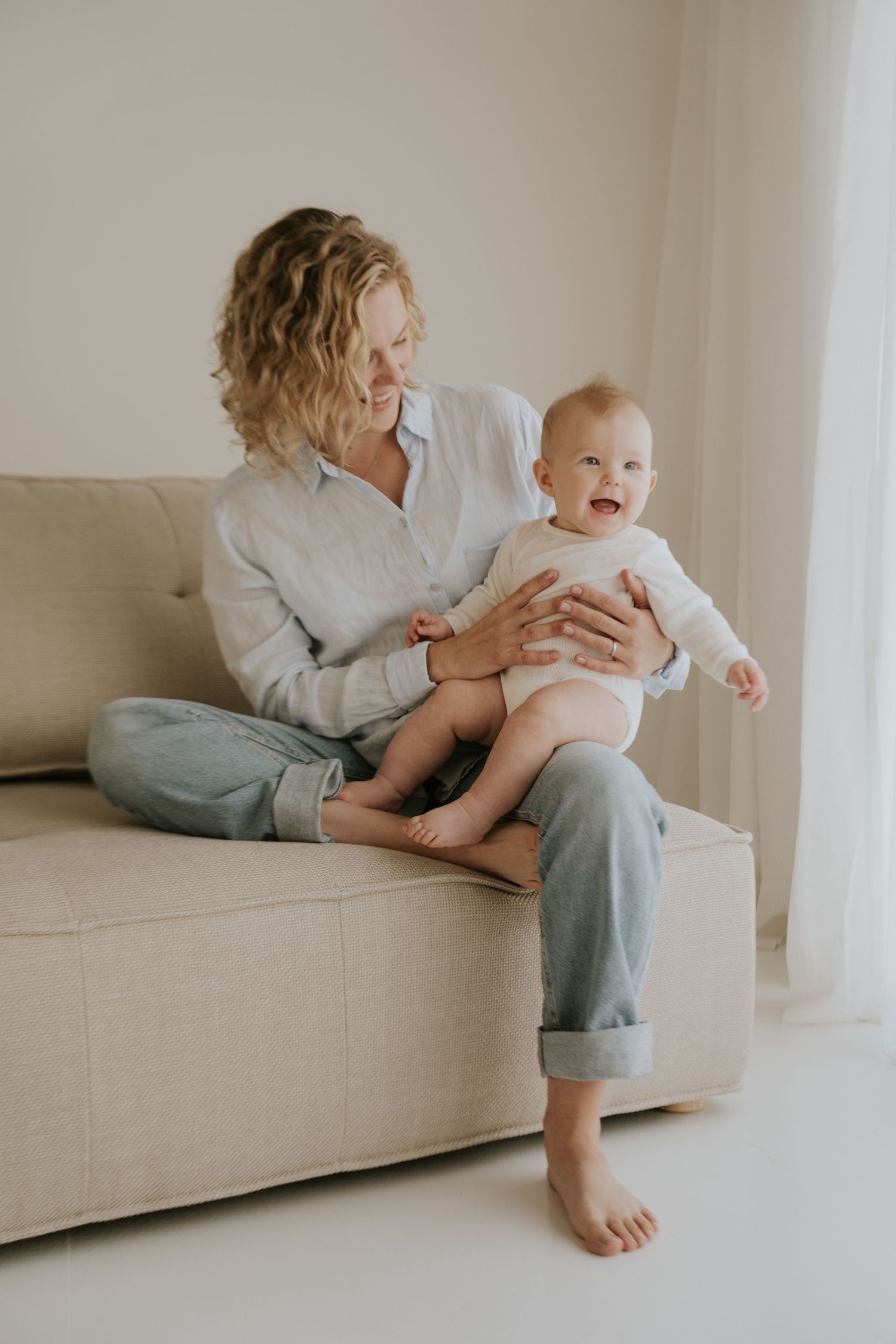Parent and baby playing together on light colored couch in minimalist setting.