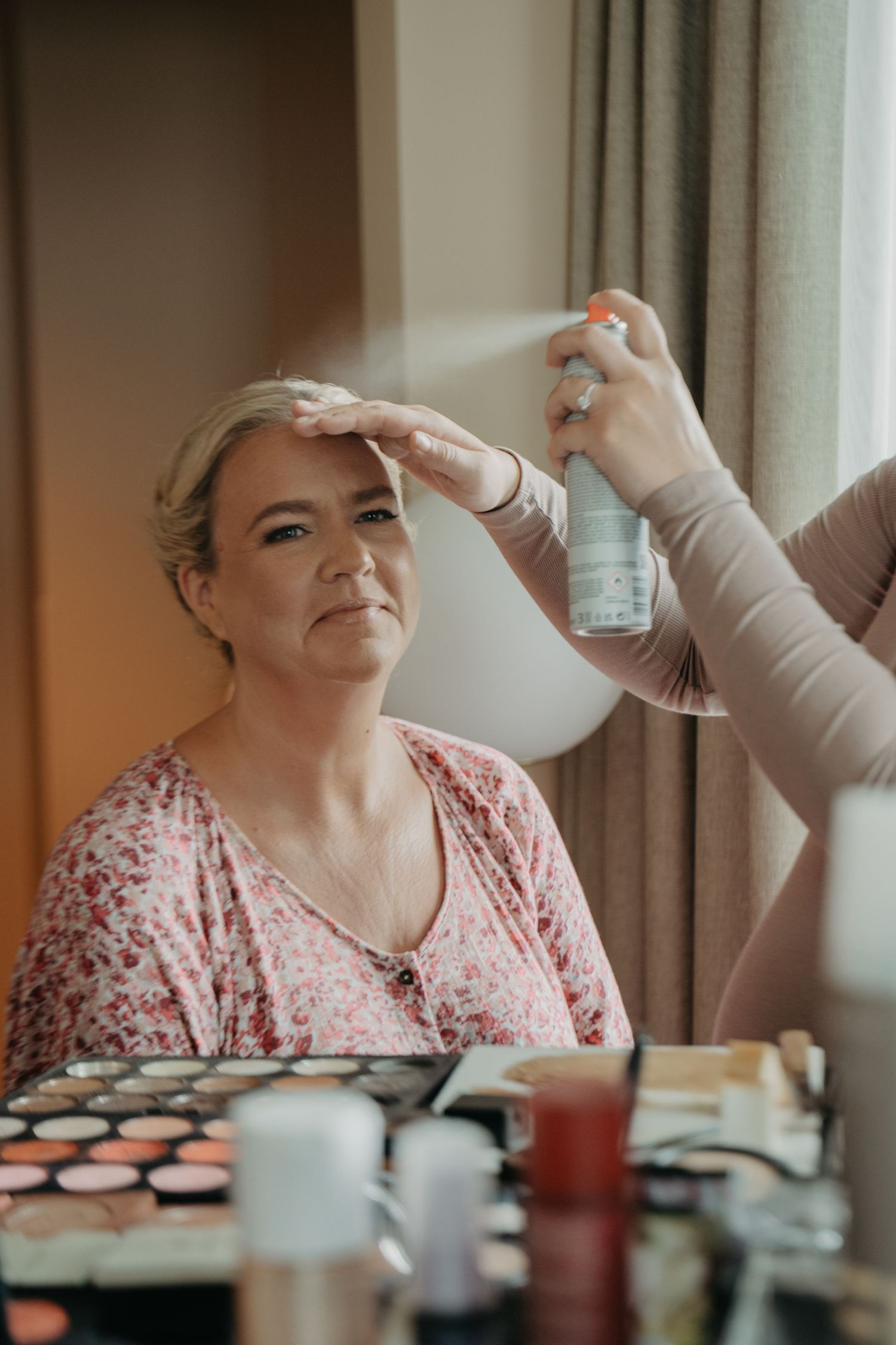 A series of photos showing someone getting their makeup professionally applied while sitting by a window.