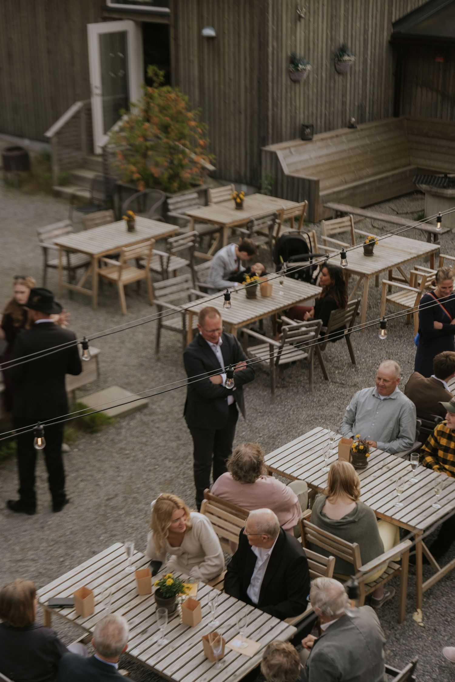 Guests gather at outdoor restaurant tables with wooden benches in a courtyard setting.