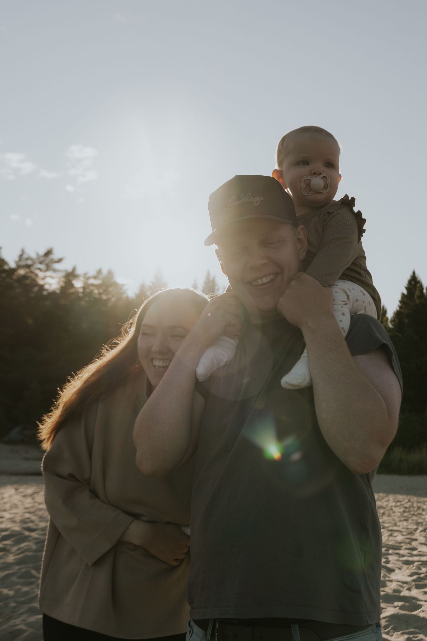 A backlit family photo on the beach with sun flare creating a warm, intimate atmosphere.