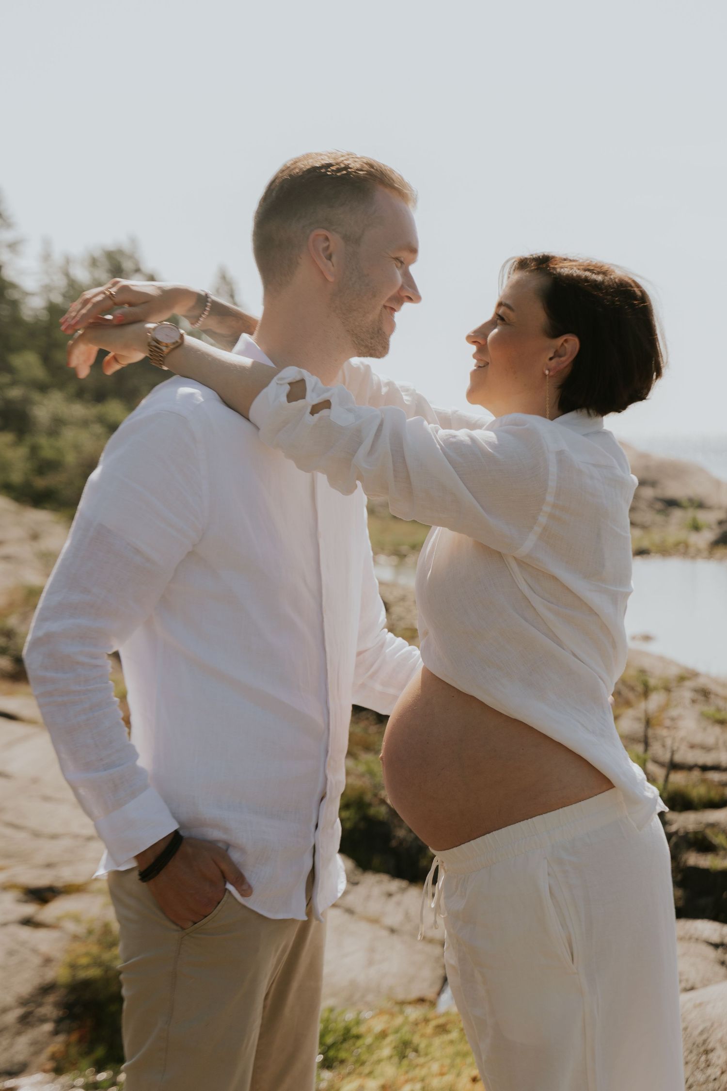 A couple in white outfits shares intimate moments on a rocky beach during a romantic photoshoot.